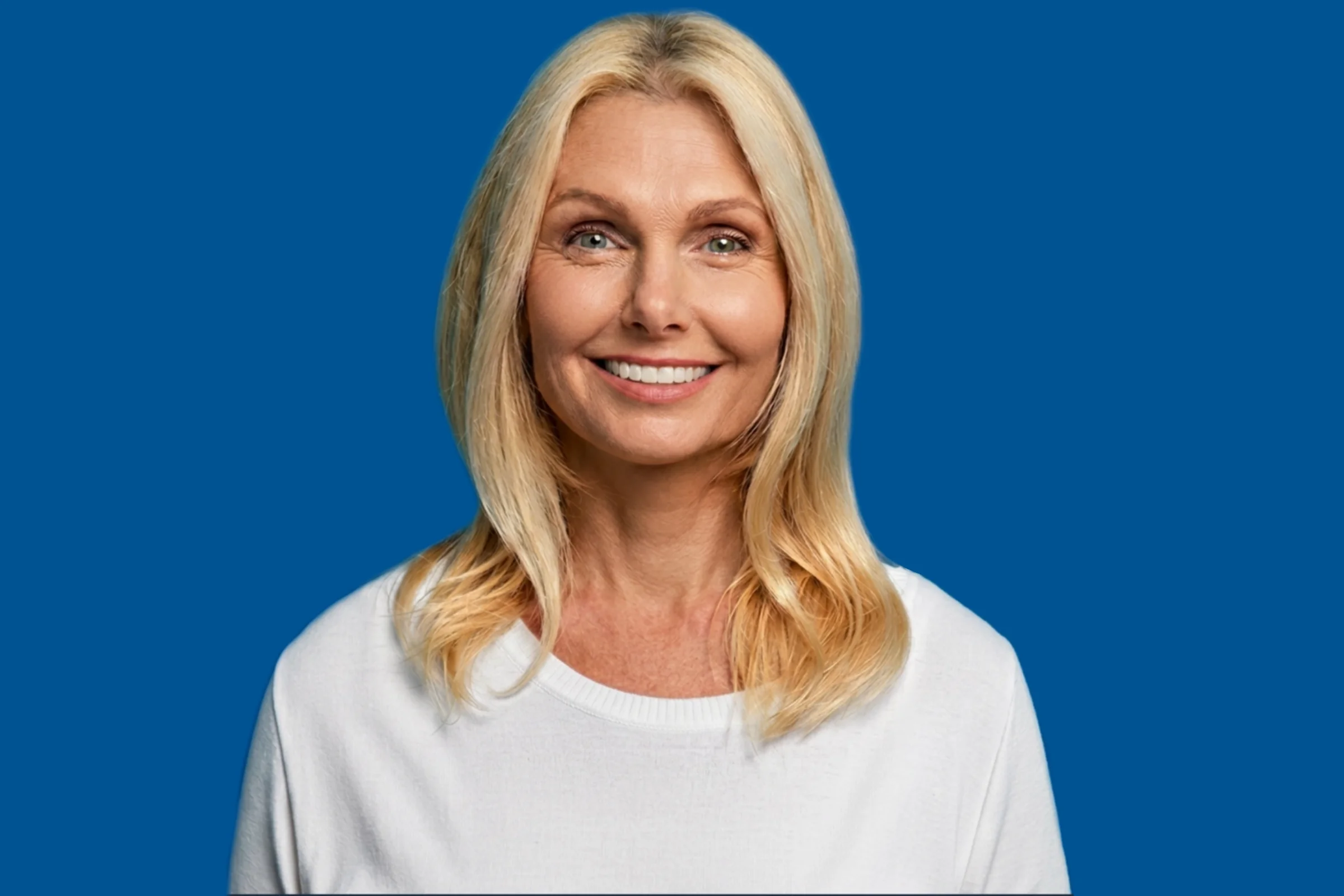 Smiling middle-aged blonde woman with shoulder-length hair wearing a white sweater against blue background.