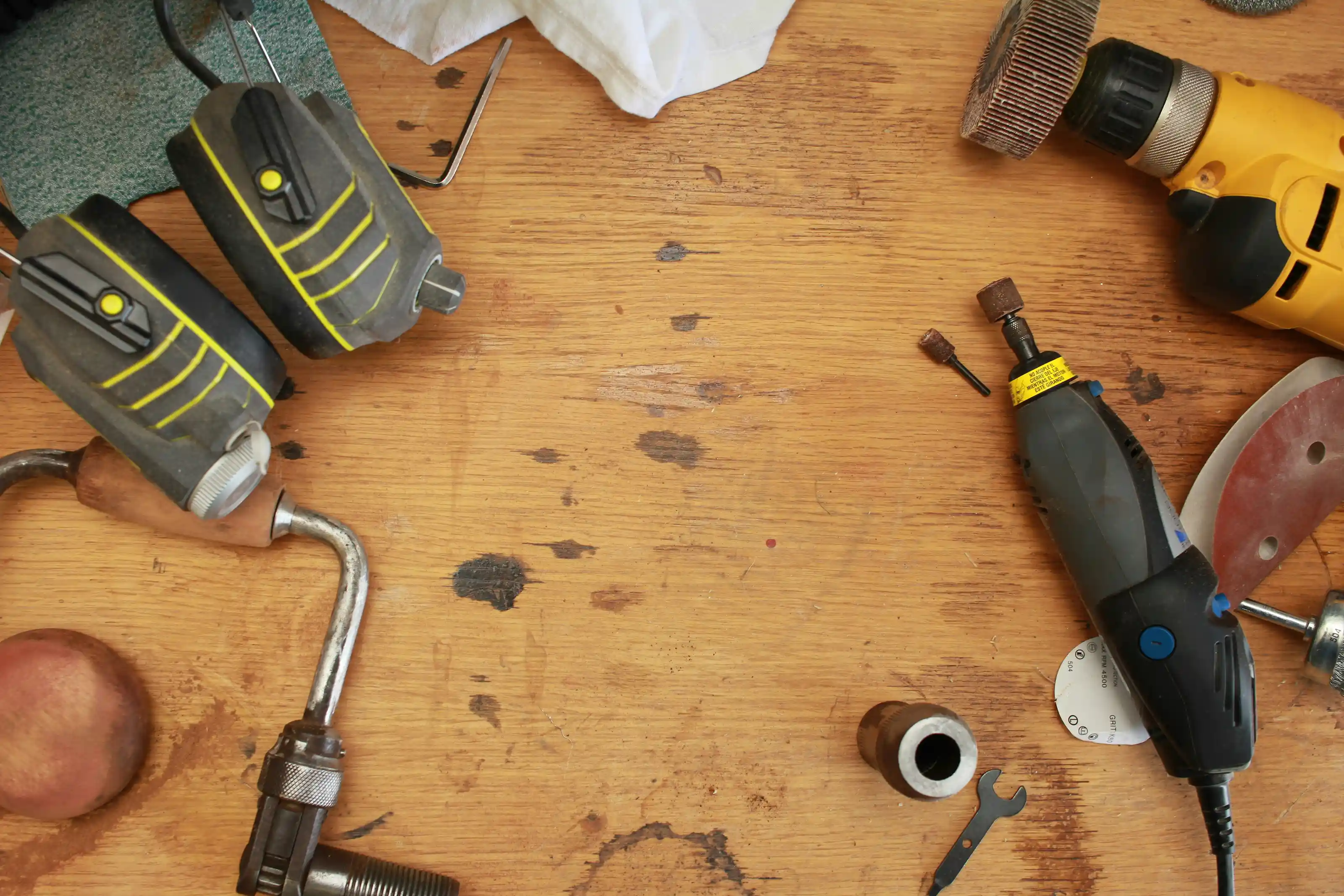 Workbench with various hand tools and electric polishing and grinding tools scattered on a wooden surface.