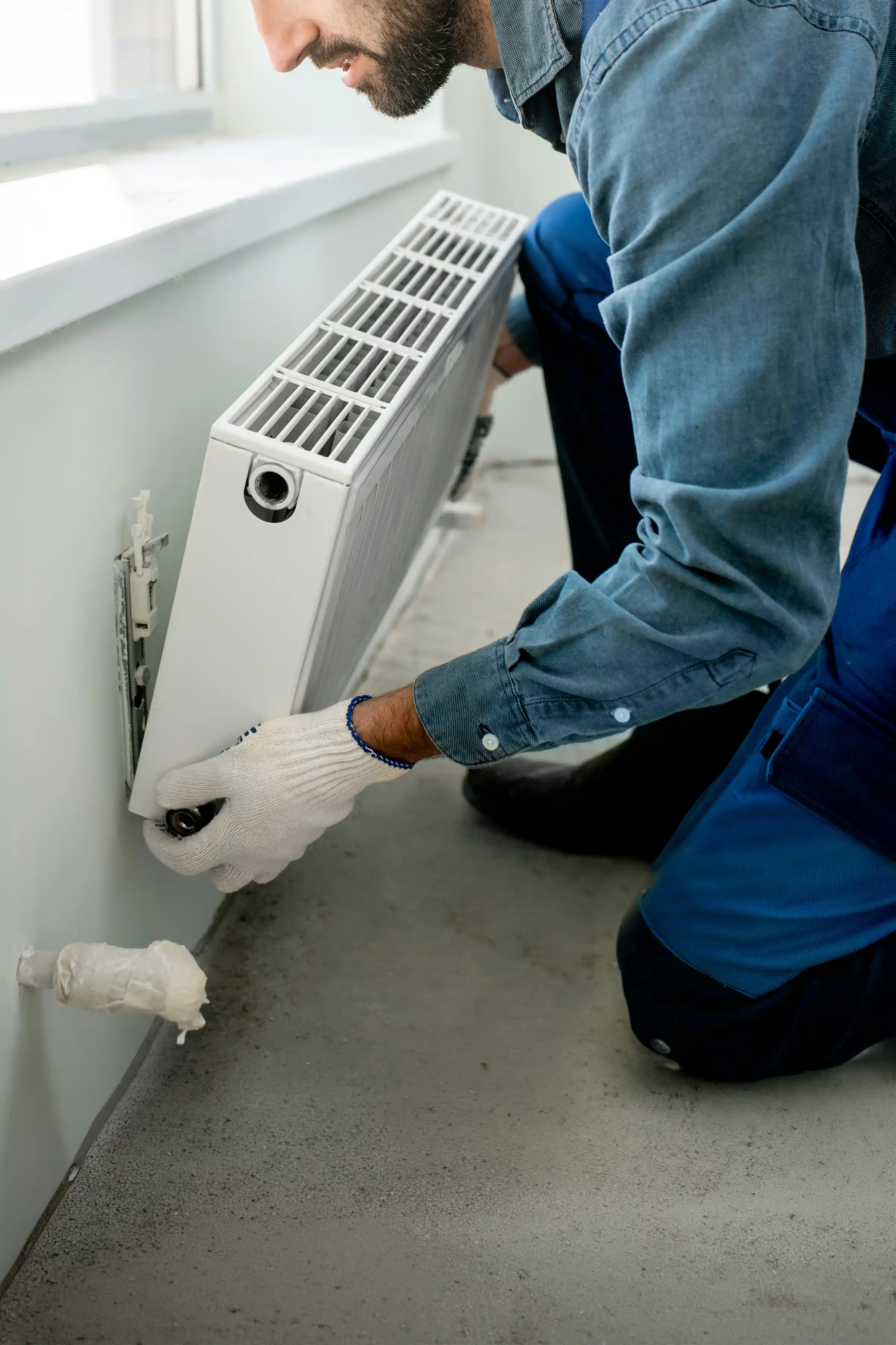 Person wearing yellow gloves and blue apron holding a blue bucket in one hand and a mop in the other indoors.