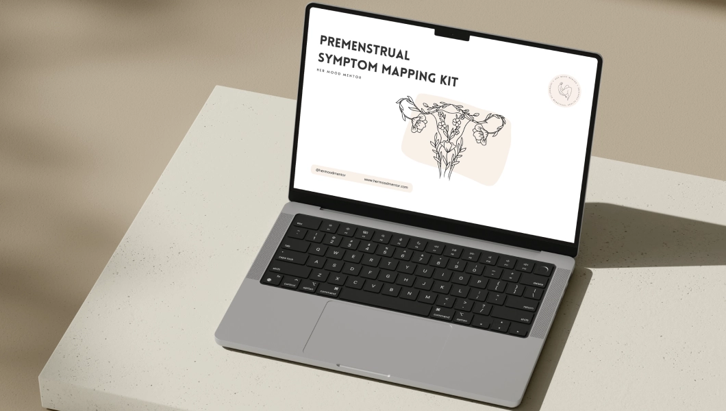 Open laptop on a beige surface displaying a screen with the text 'The PMDD Clarity Kit: Finally Understand What Your Body Is Trying to Tell You' and a woman in white sitting on the right side of the screen.