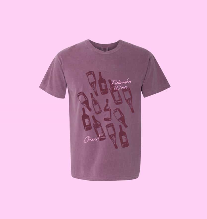 Purple t-shirt with burgundy wine bottle illustrations and text saying 'Nebraska Wines' and 'Cheers!'.