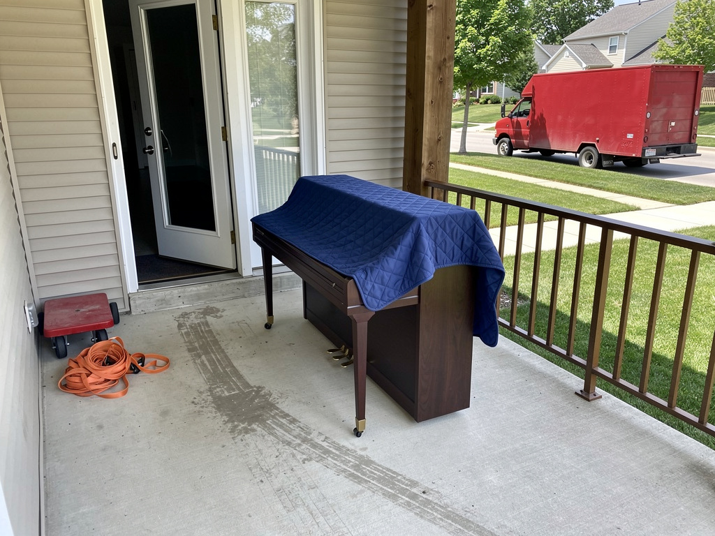 Piano wrapped in moving blankets on front porch ready for pickup