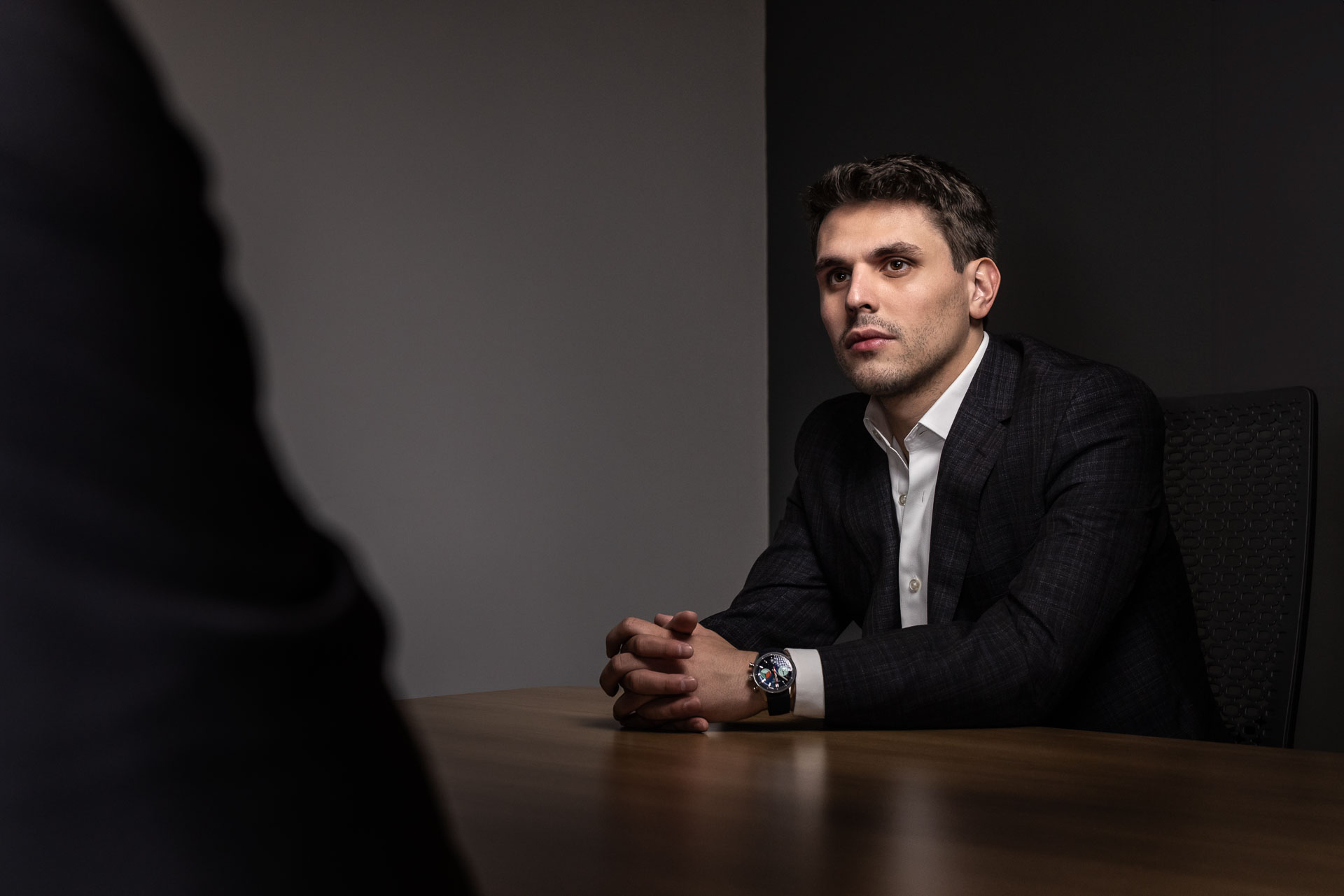 Charles W. Garcia in a dark suit and white shirt sitting at a wooden table looking attentive.
