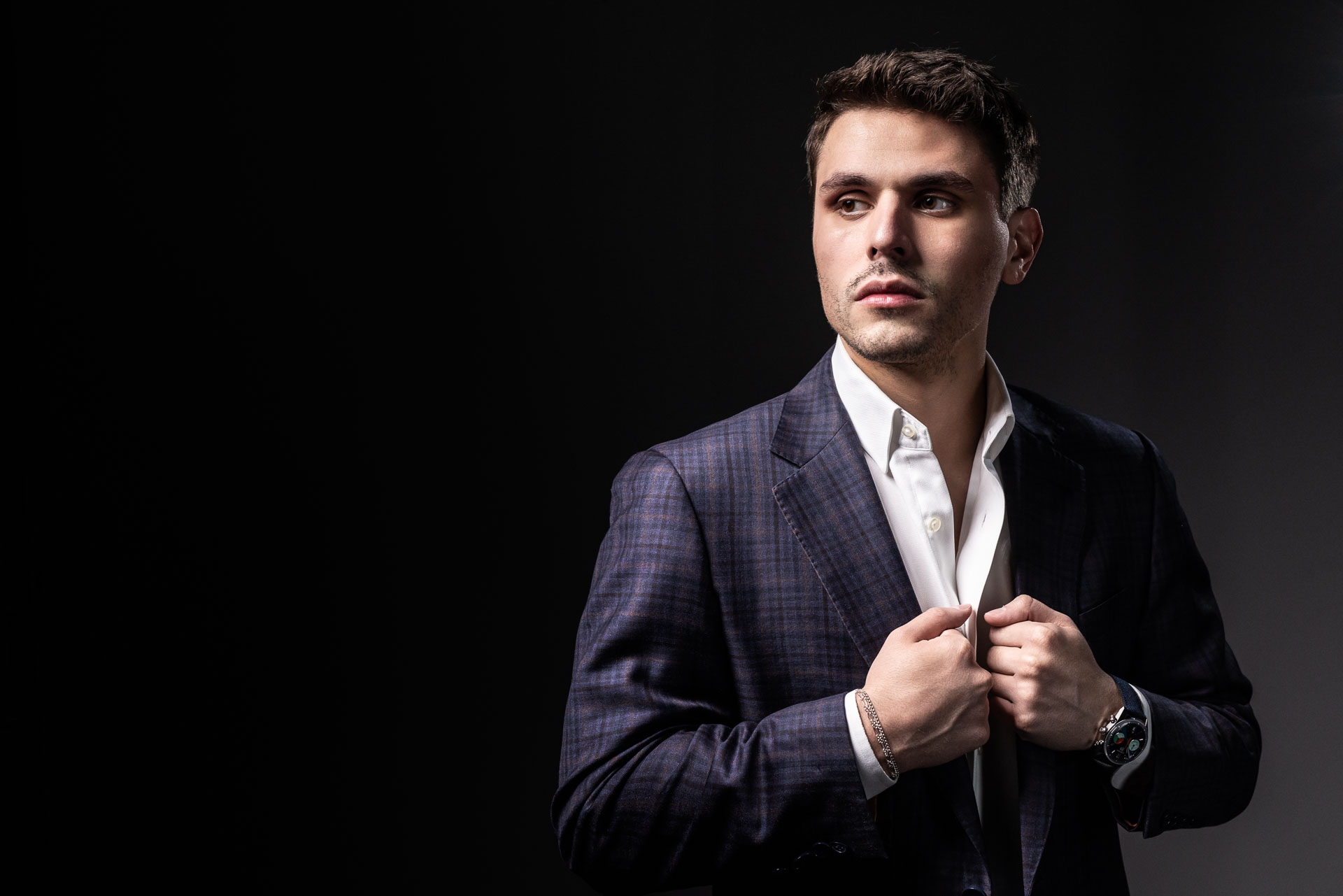 Charles W. Garcia in a dark checkered suit and white shirt adjusting his jacket against a dark background.