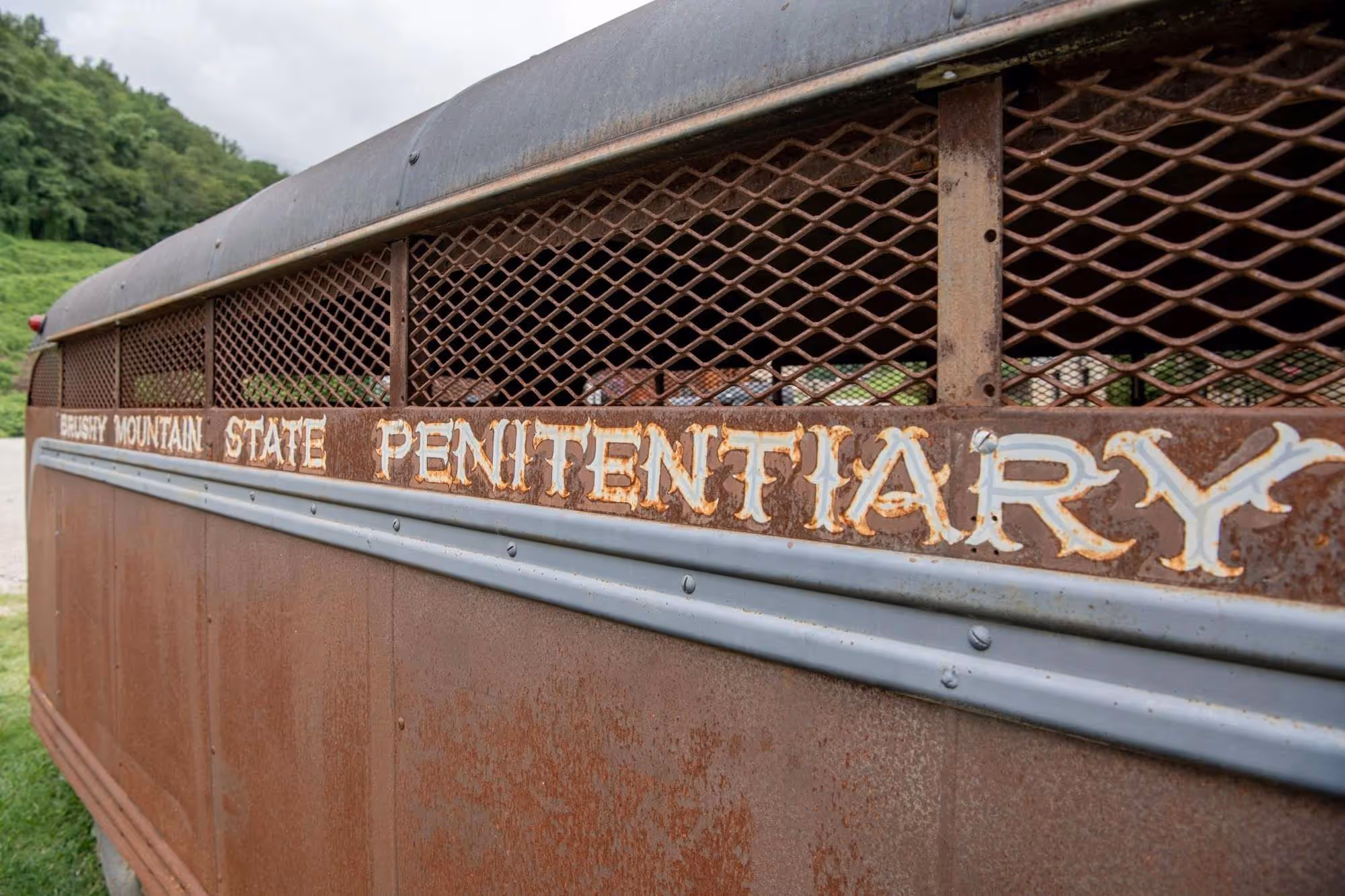 Rusty metal side of a prison transport vehicle with the words 'Brushy Mountain State Penitentiary' worn and faded.