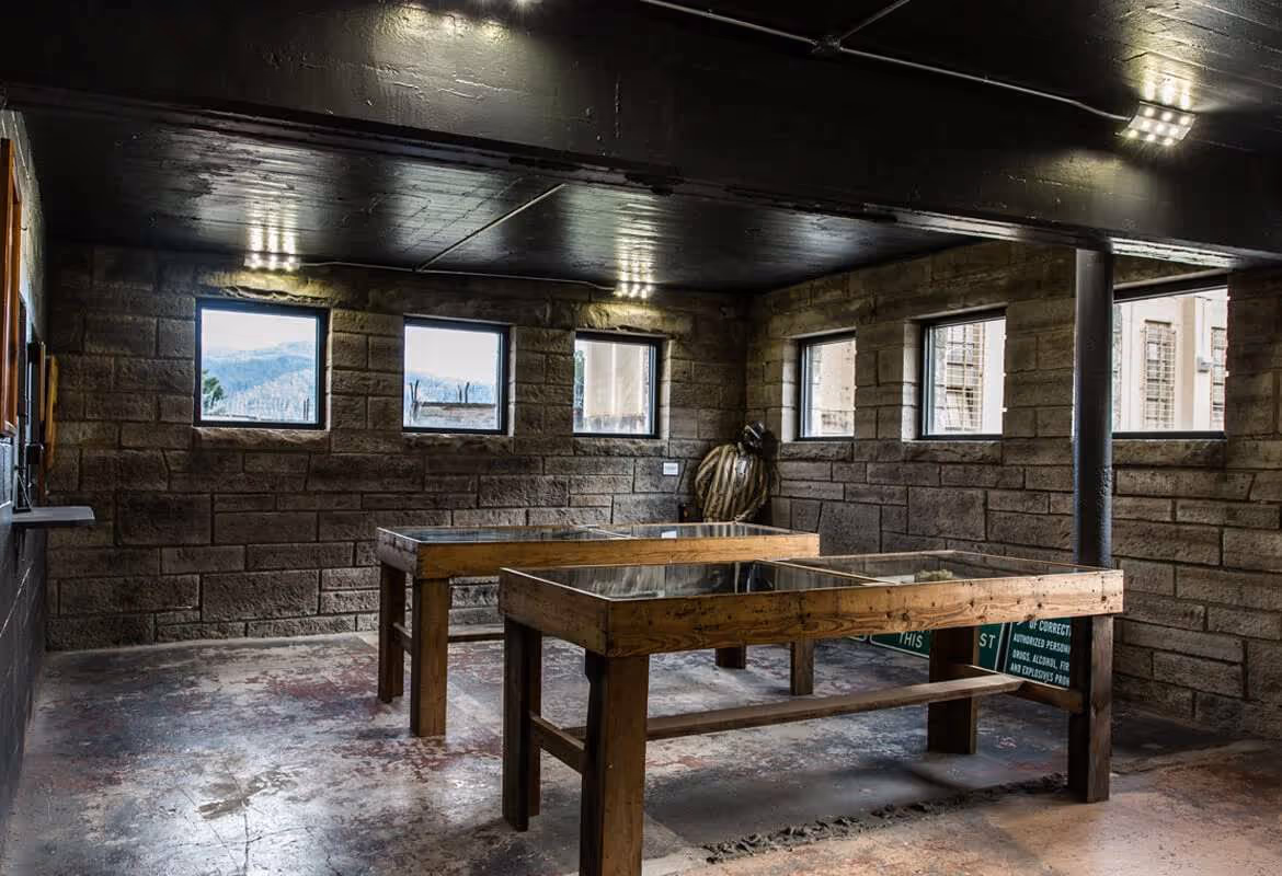 Interior of a dimly lit museum room with stone walls, featuring two wooden display cases with glass tops and a statue of a figure in the corner.