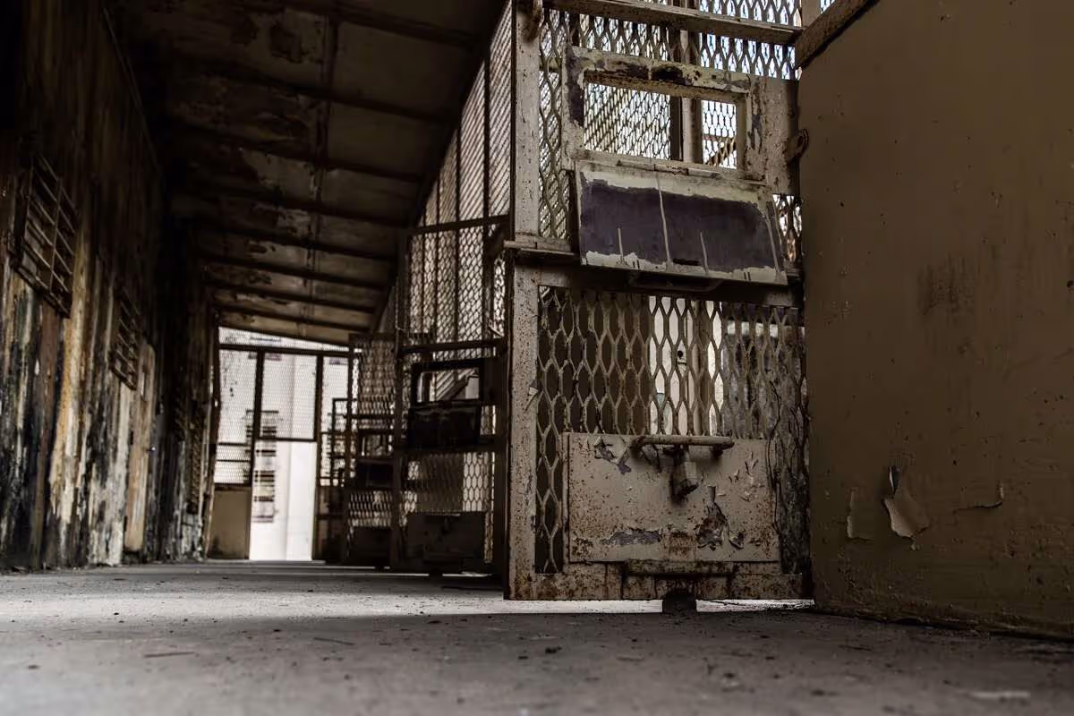 Low-angle view of an old, rusty prison corridor with peeling paint and metal barred cells.