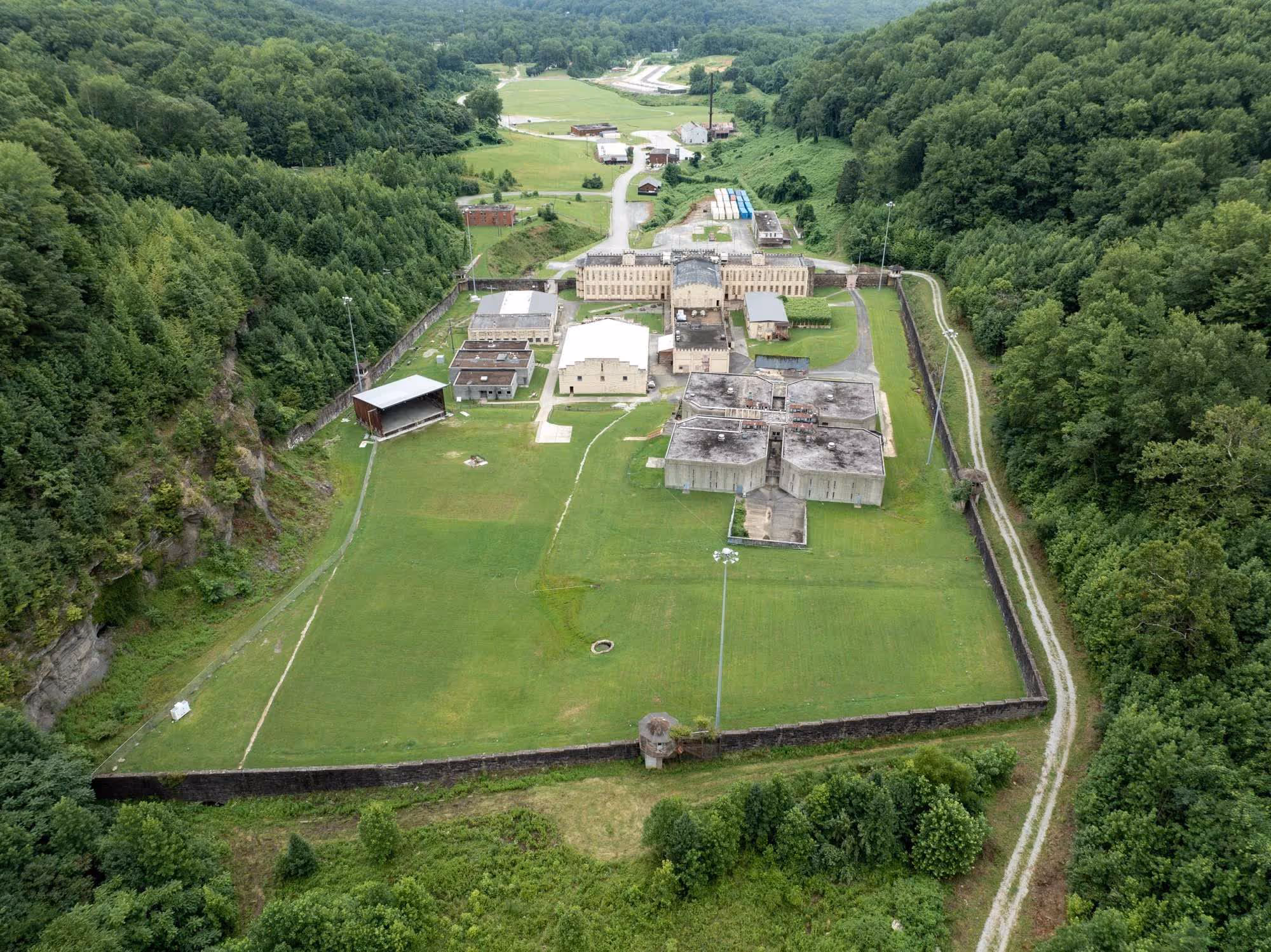 Aerial view of the prison complex surrounded by green forested hills with multiple buildings and tall stone fence walls.