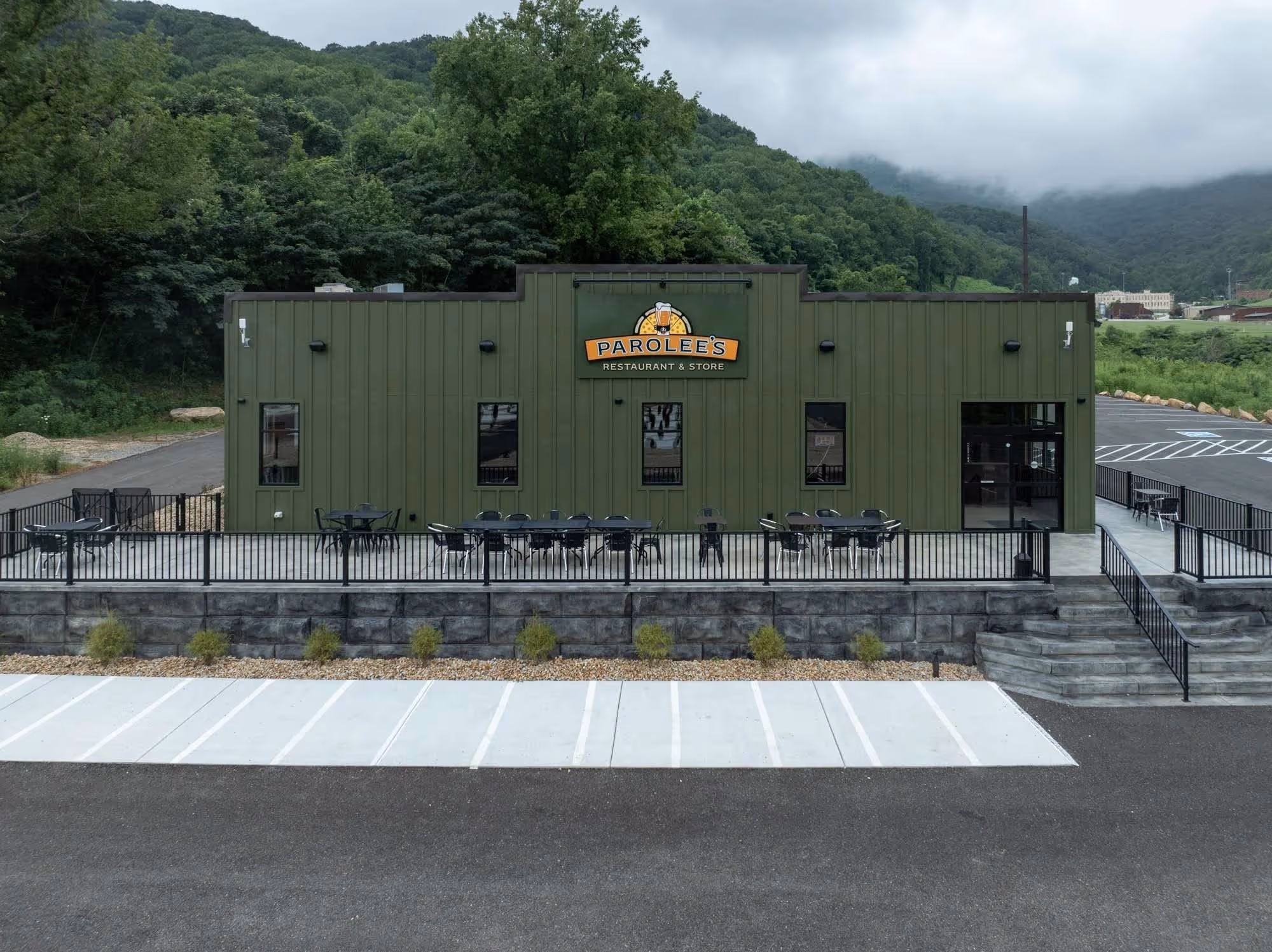 Green building with 'Parolee's Restaurant & Store' sign, outdoor patio seating, and mountainous forest background under cloudy sky.