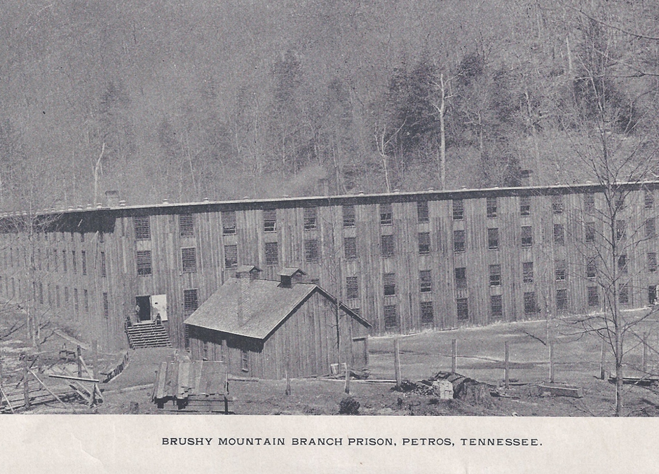 Historical black and white photo of Brushy Mountain Branch Prison in Petros, Tennessee, showing long wooden prison building and a smaller wooden structure in front.