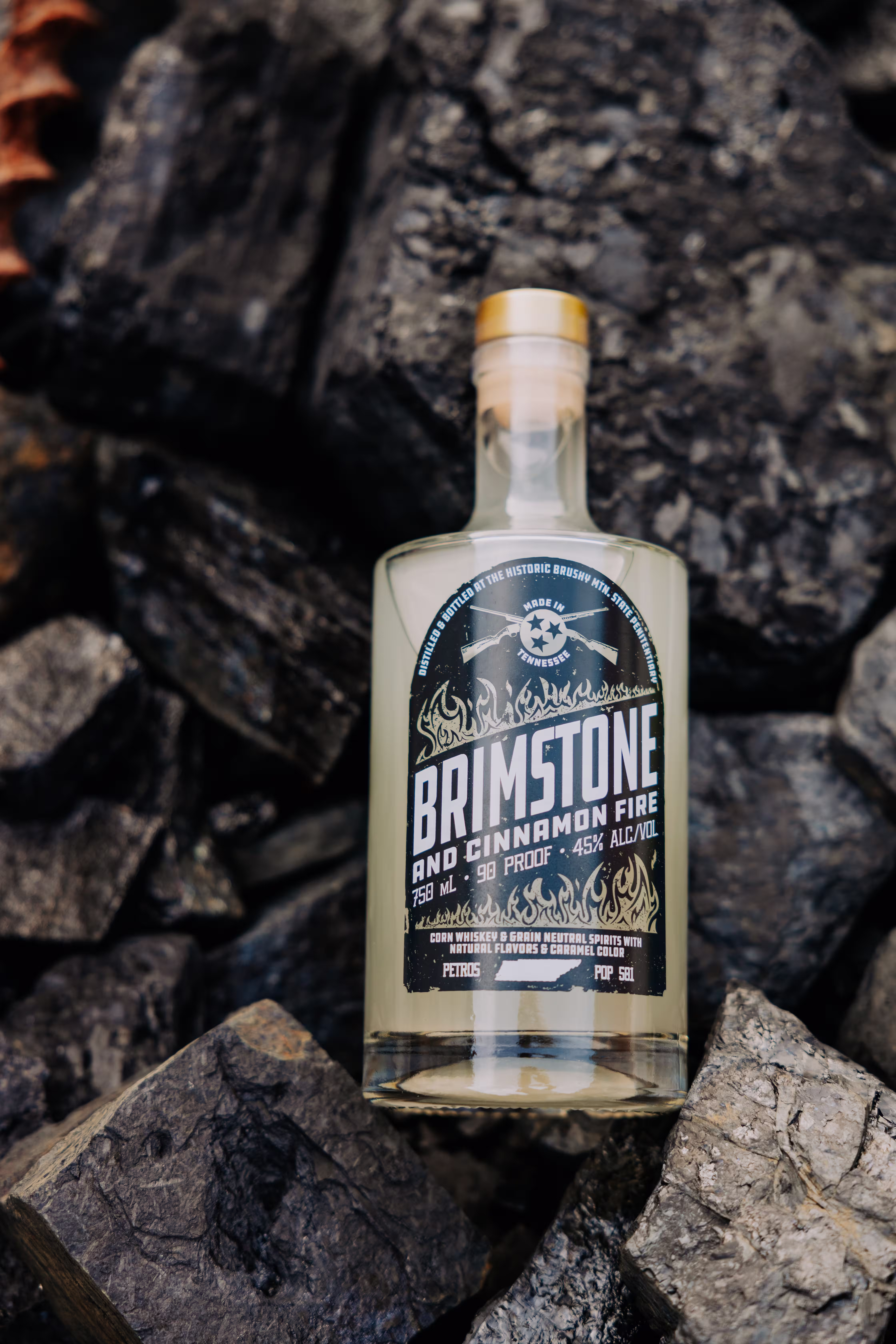 Bottle of Brimstone, Cinnamon Fire whiskey on dark charcoal rocks.
