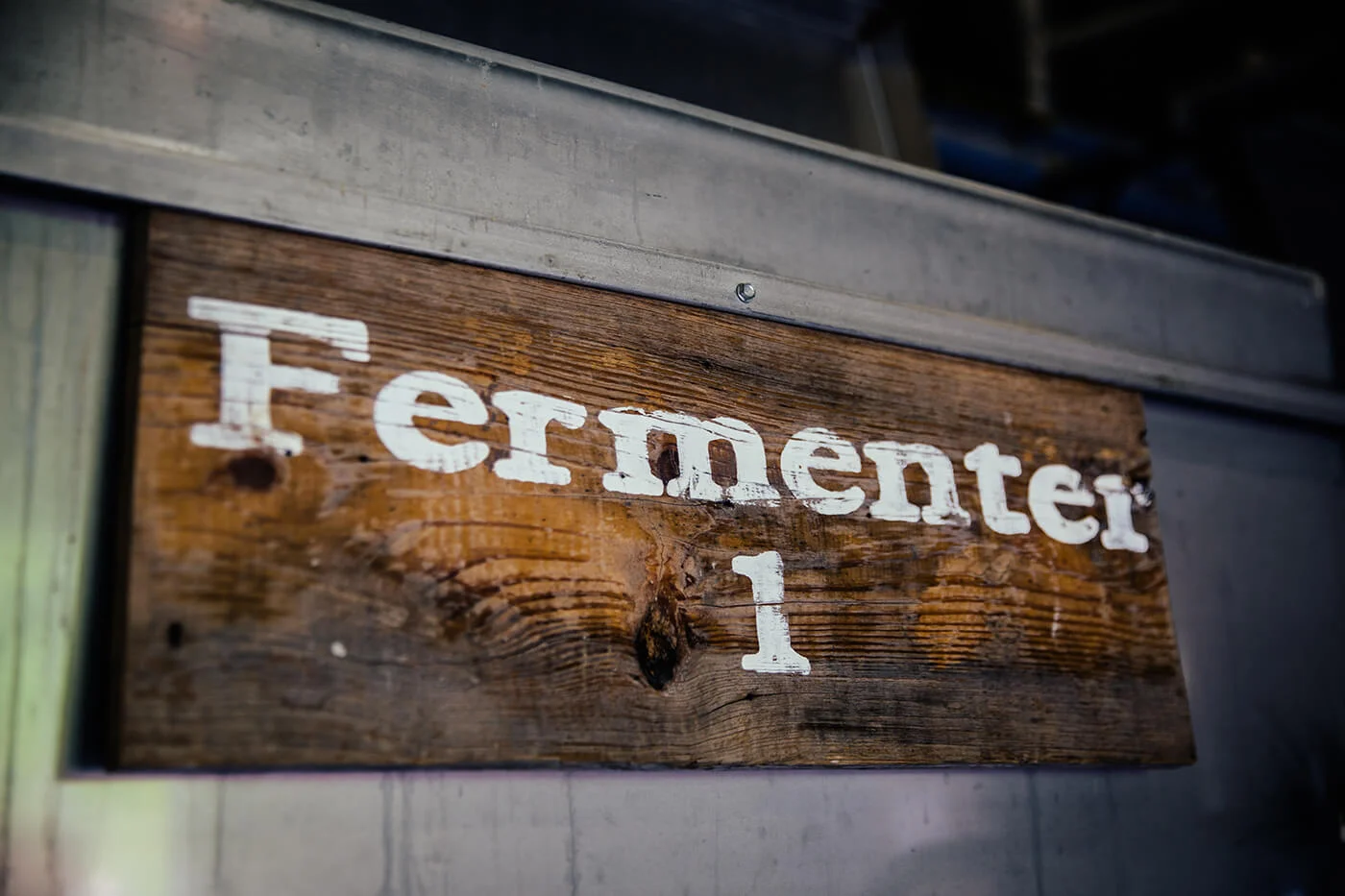 Wooden sign with white letters spelling 'Fermenter 1' mounted on a wall.
