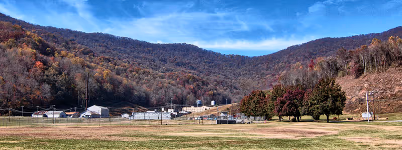 Wide view of a valley with a fenced area and buildings surrounded by wooded hills with autumn foliage under a blue sky.