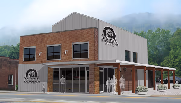 Two-story Coal Creek Miners Museum building with brick and gray metal siding, a front awning, and people walking near the entrance.