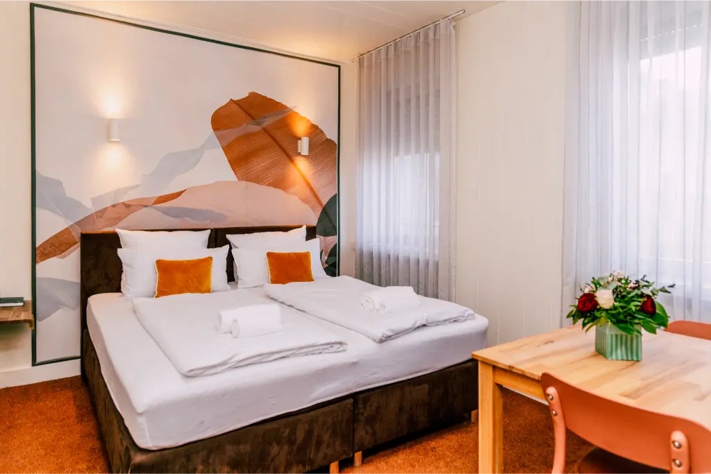 Doppelzimmer mit Blatt-Wandbild, Esstisch und Blumenstrauß im Hotel Kleiner Markt Saarlouis