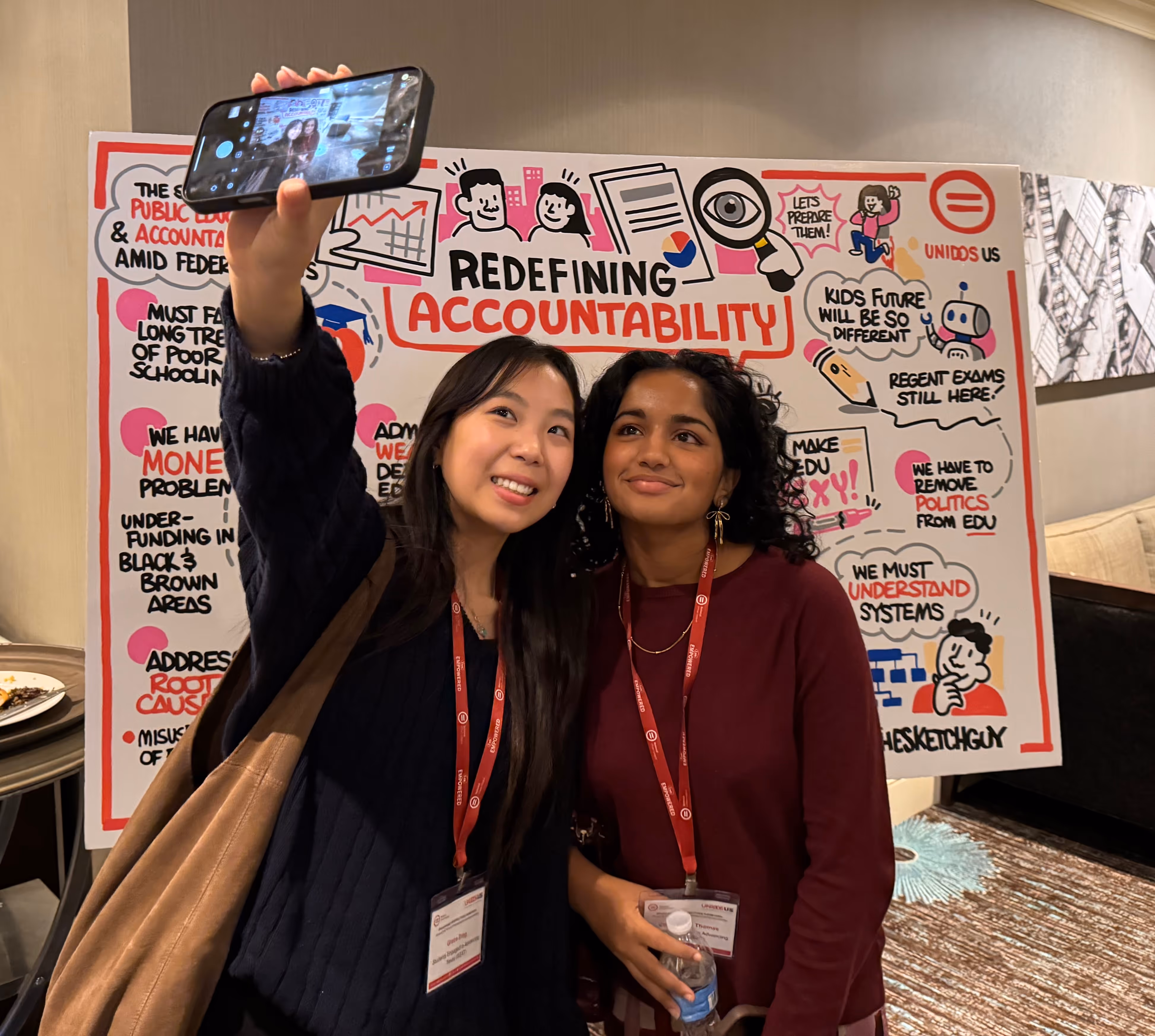 Two SEAT leaders taking a selfie in front of a colorful poster about redefining accountability.