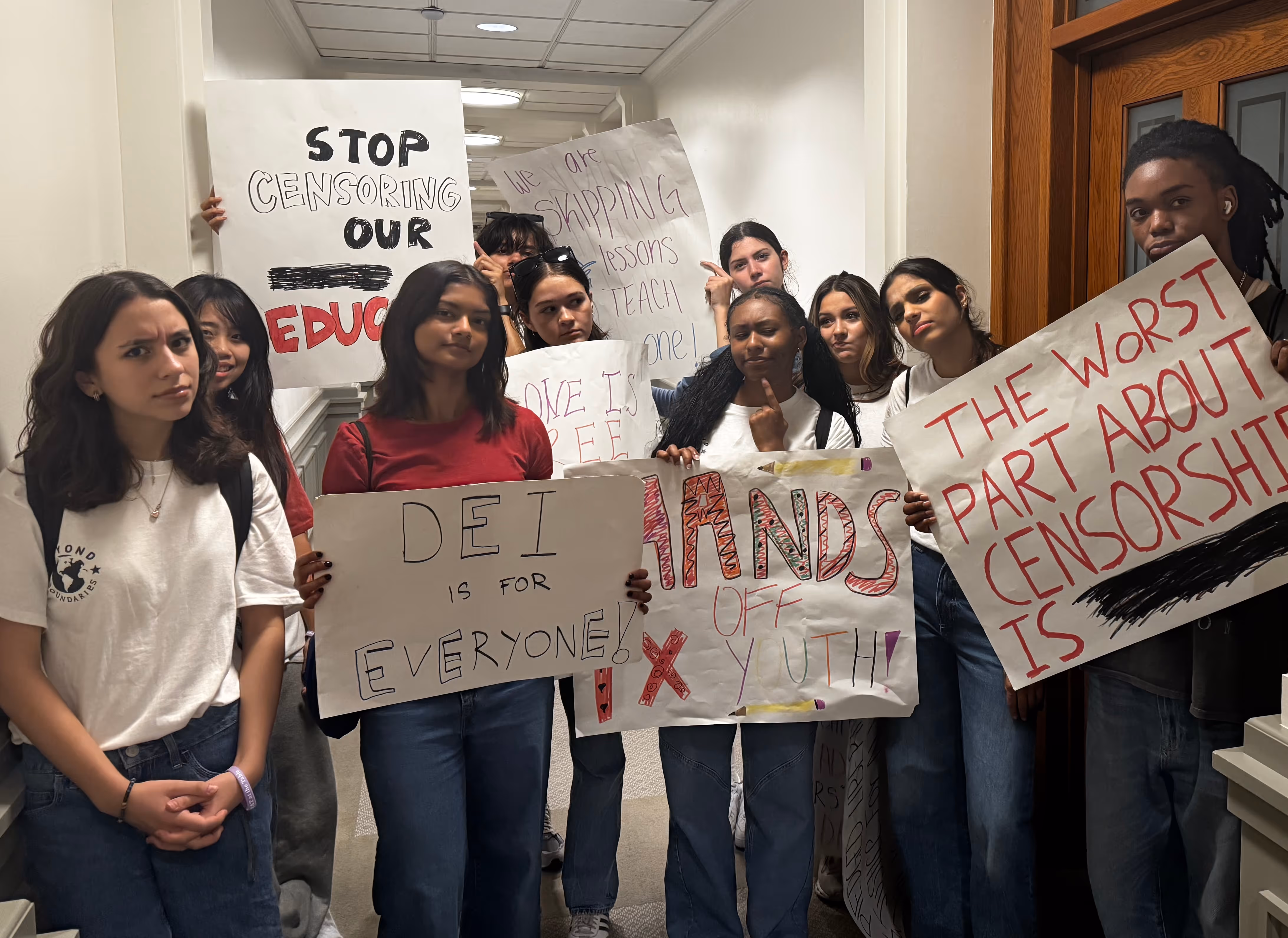Group of diverse young people holding protest signs against censorship in a hallway of the Texas Capitol.