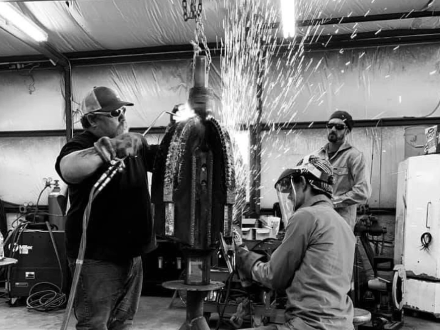 Three men welding PDC HDD Reamer in Terra Rock Bits industrial workshop in Texas.
