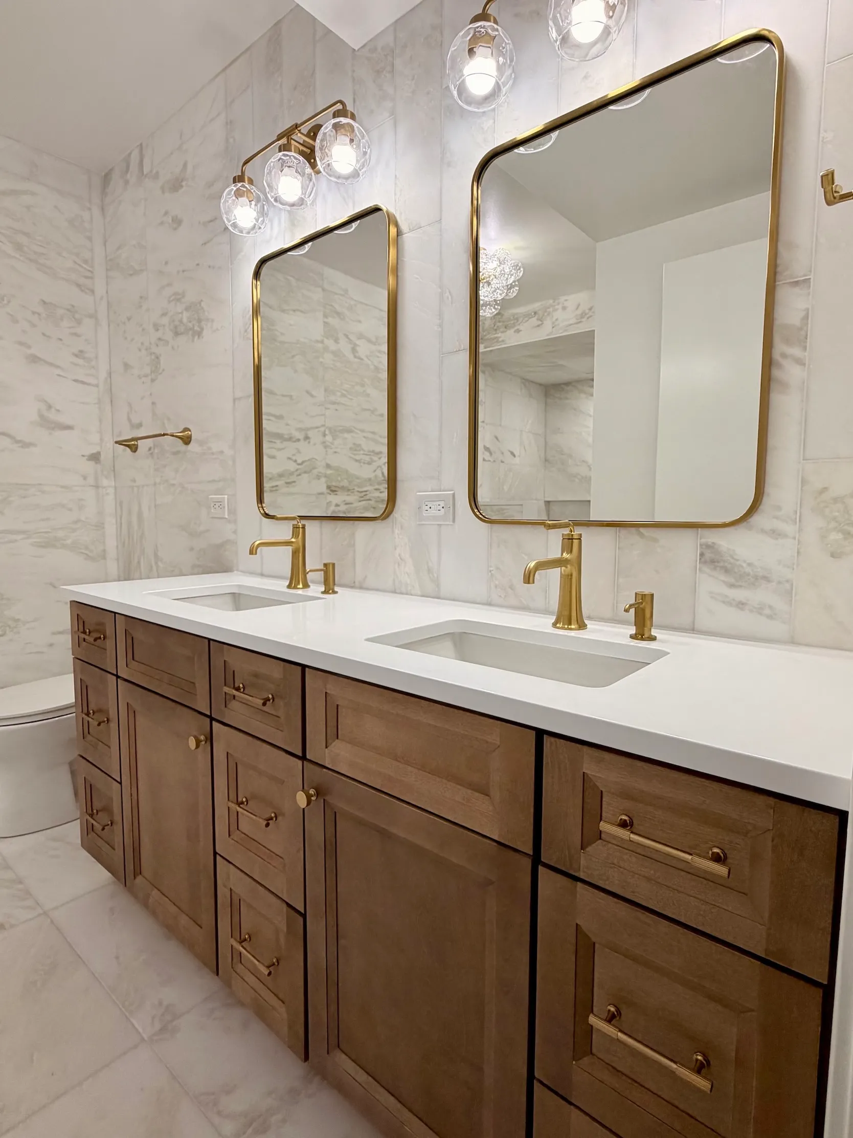 Remodeled bathroom with dark wood double sink vanity and brass-trimmed mirrors and fixtures by Wood Contracting