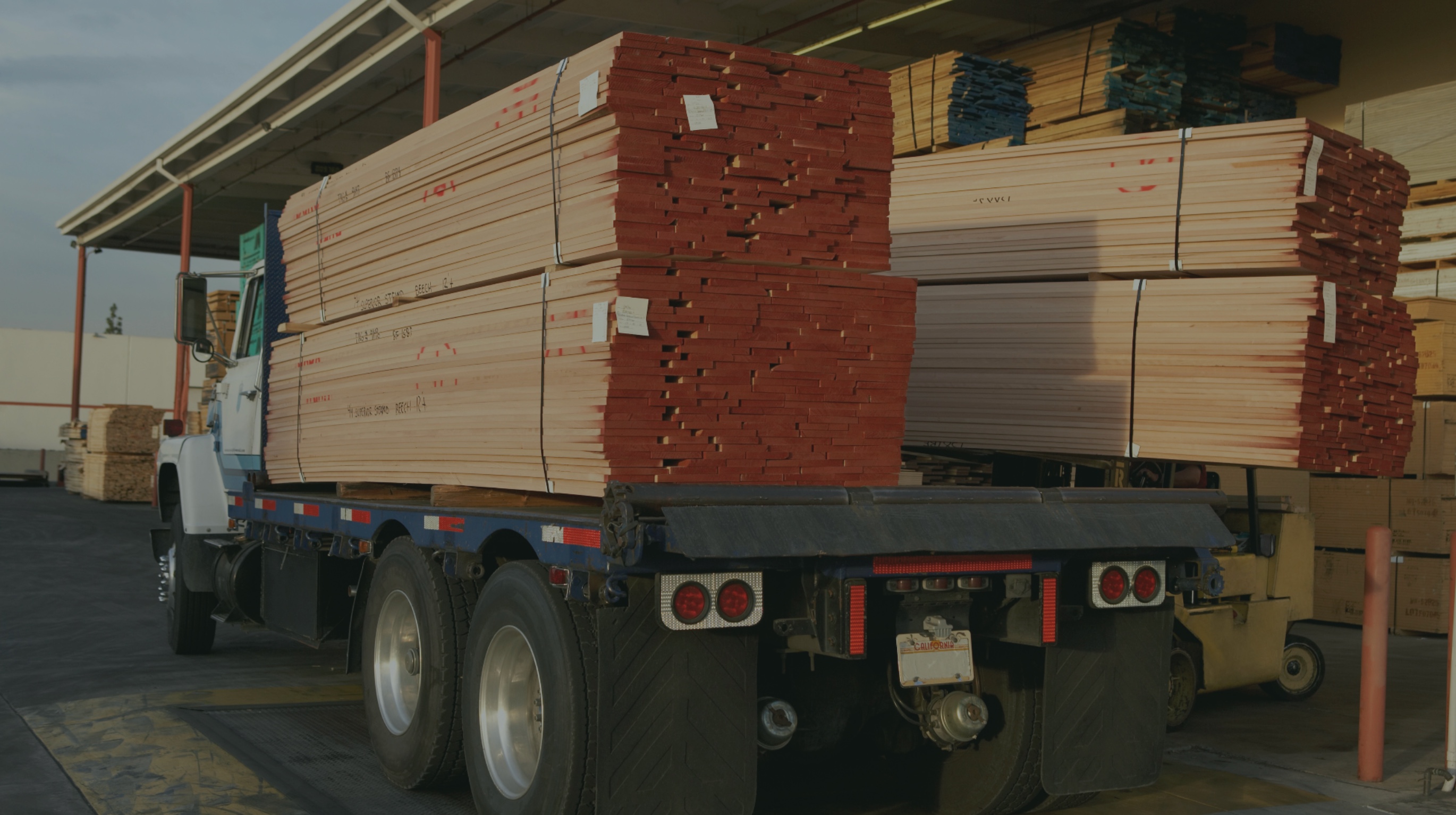 Flatbed truck loaded with large bundles of lumber parked near a warehouse.