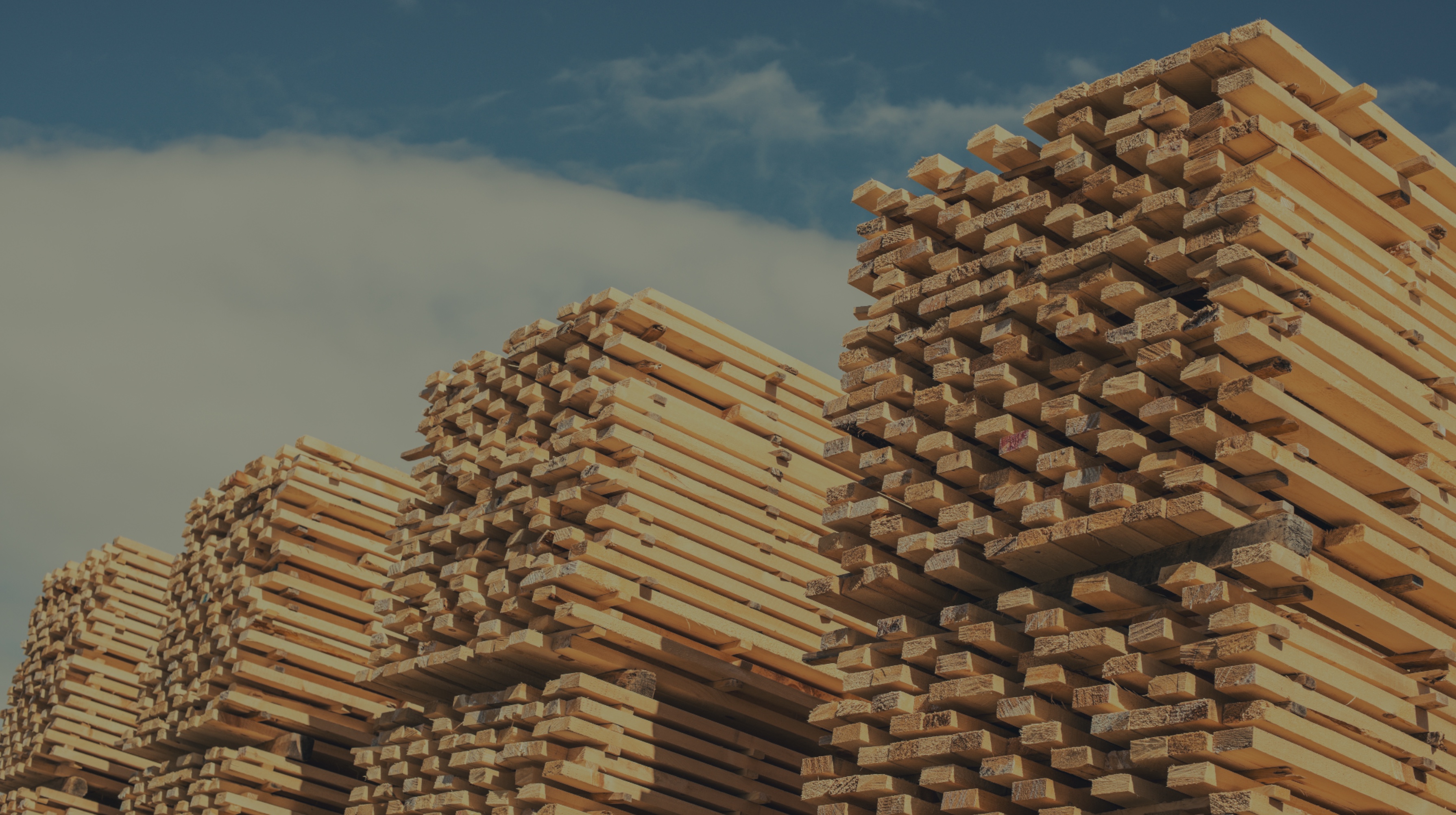 Stacks of neatly piled lumber under a partly cloudy sky.