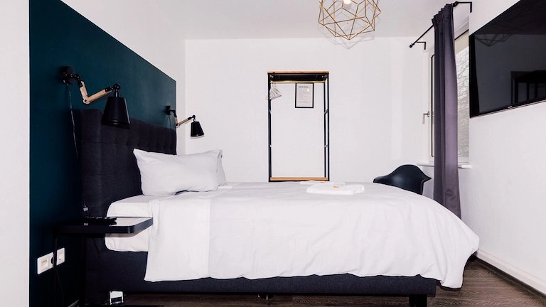 Zimmer Small mit Bett, petrolfarbener Wand und Gold-Pendelleuchte im Boutiquehotel Palmenbad Kassel