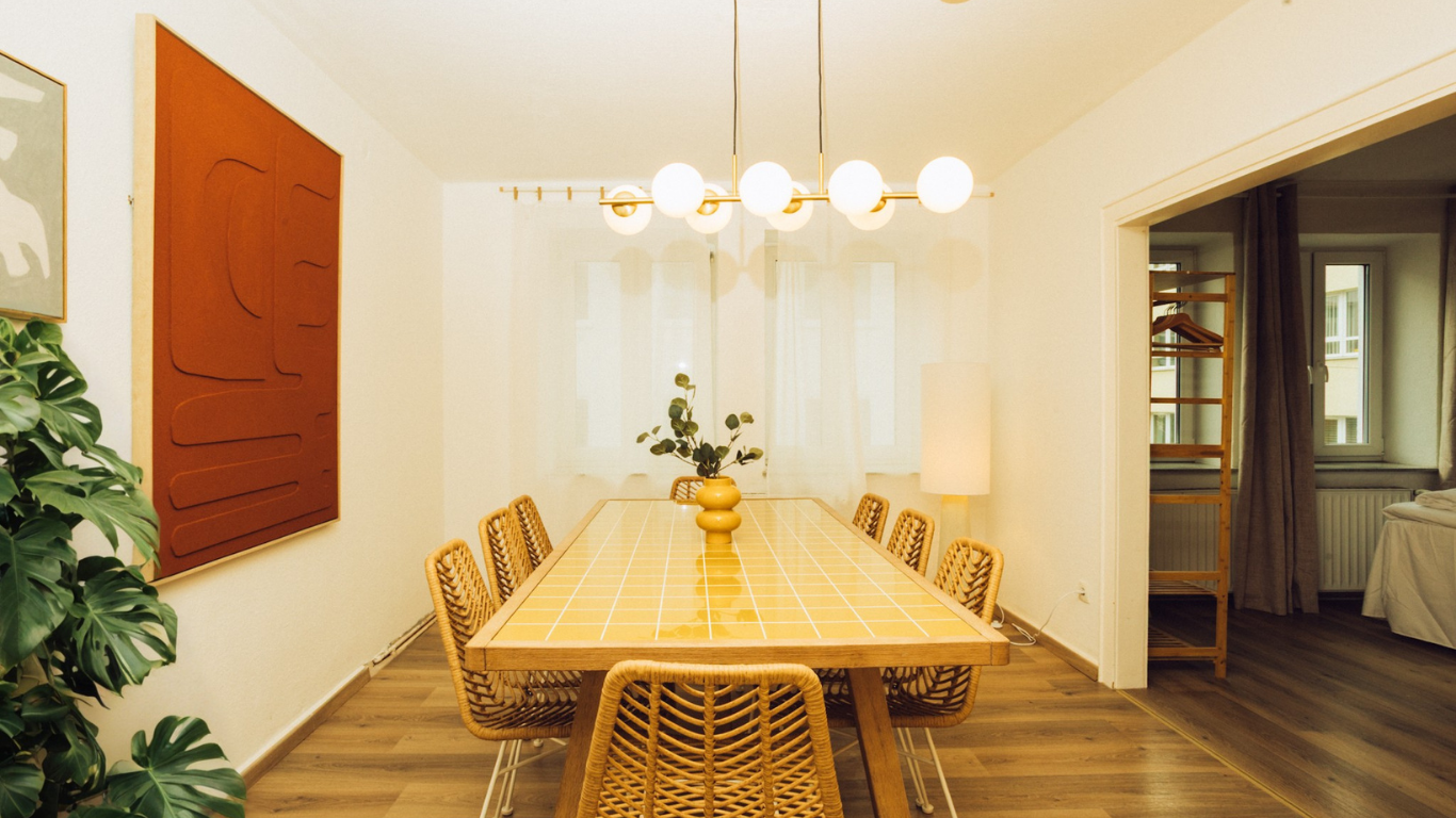 Essbereich mit gelbem Fliesentisch, Rattanstühlen und Monstera in den Stadtpark Apartments Kassel