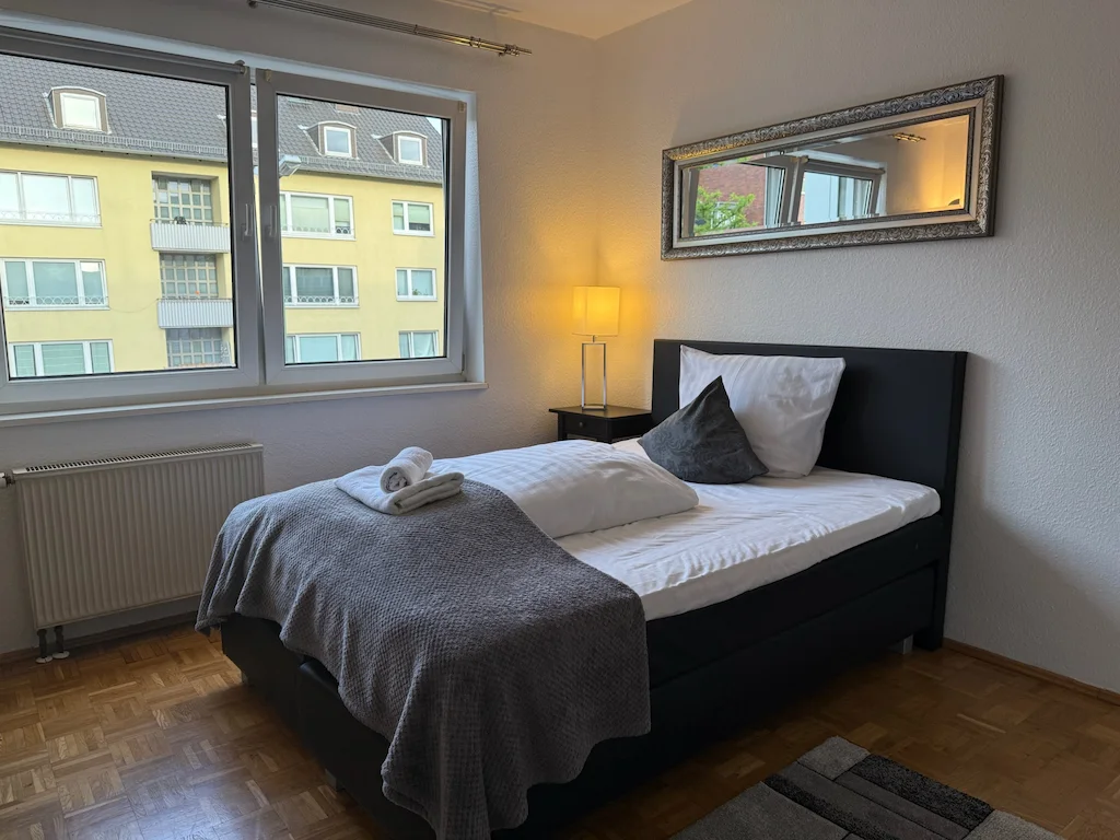 Helles Zimmer im Boardinghaus Kassel mit Doppelbett, Wandspiegel und Blick auf Nachbargebäude.
