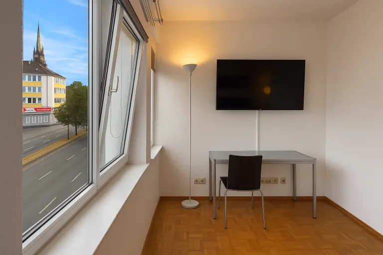 Arbeitsplatz mit Schreibtisch und TV im Boardinghaus Kassel, Fensterblick auf Häuser und Kirchturm.