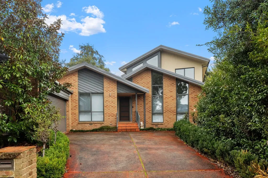 Modern two-story brick house with large windows, a driveway, and lush green shrubs on both sides.