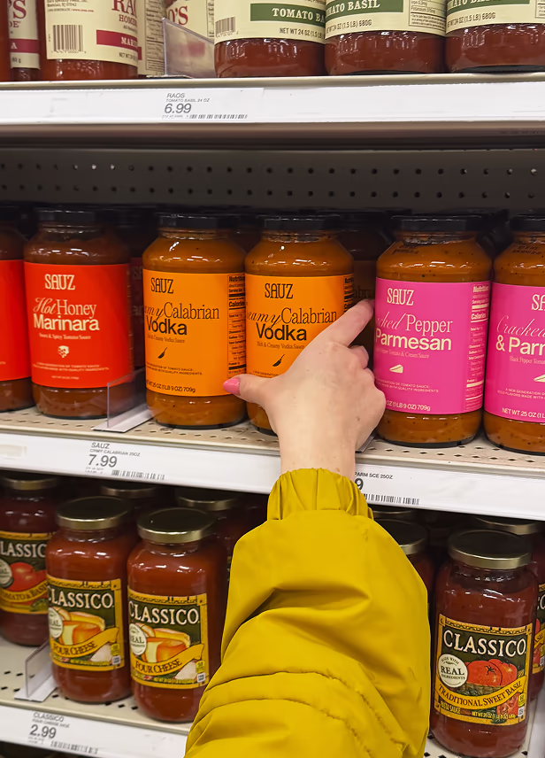 Hand reaching for pasta sauce on a retail shelf