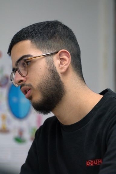Young man with glasses and short black hair wearing a black Hugo sweatshirt, looking intently to his left.
