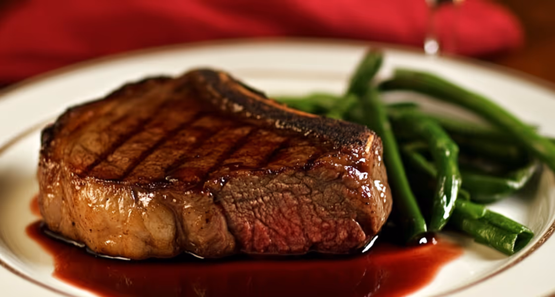 Grilled medium-rare steak with green beans on a white plate with sauce.