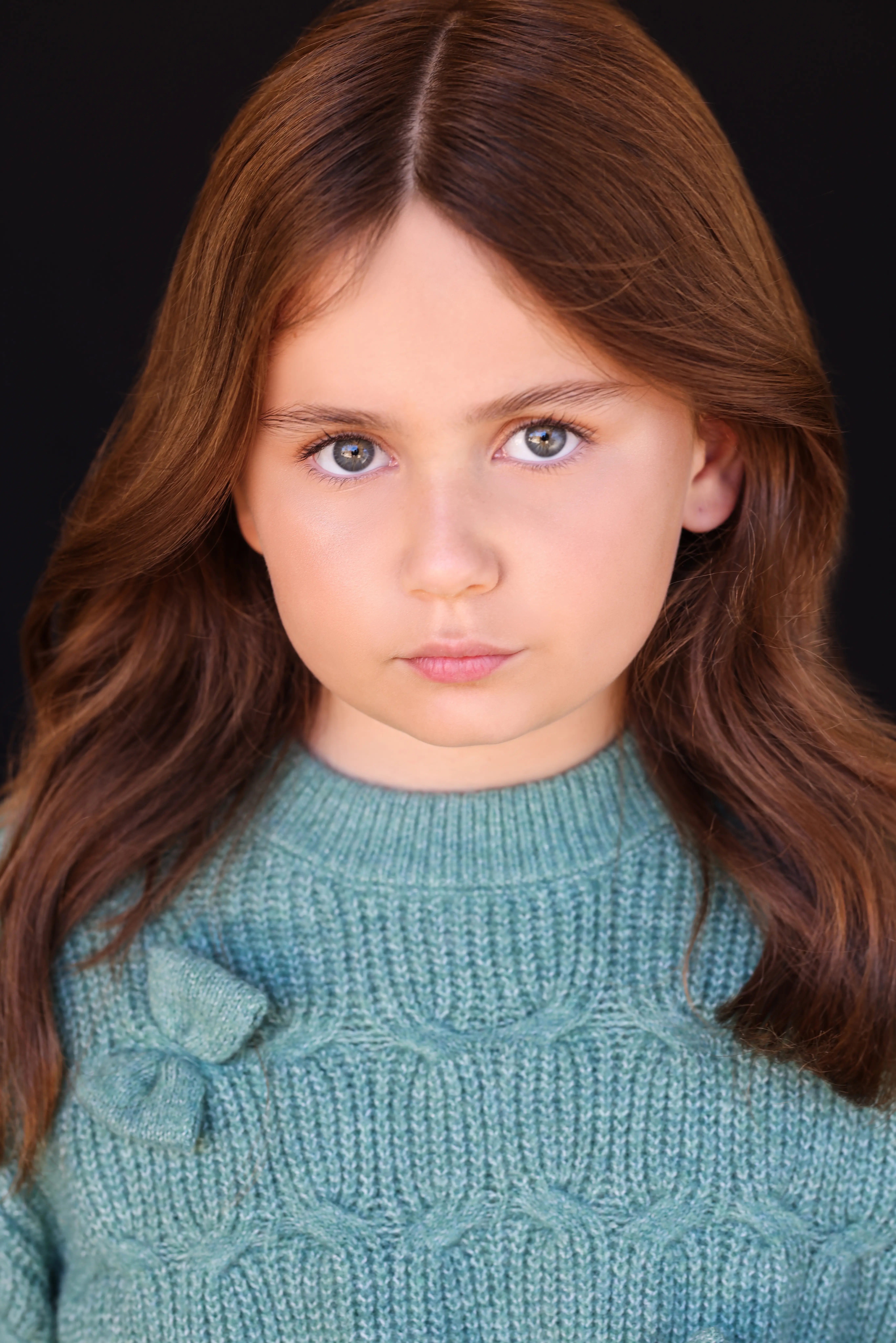 Child actress Caroline Brauner with a serious expression wearing a teal sweater against a black background