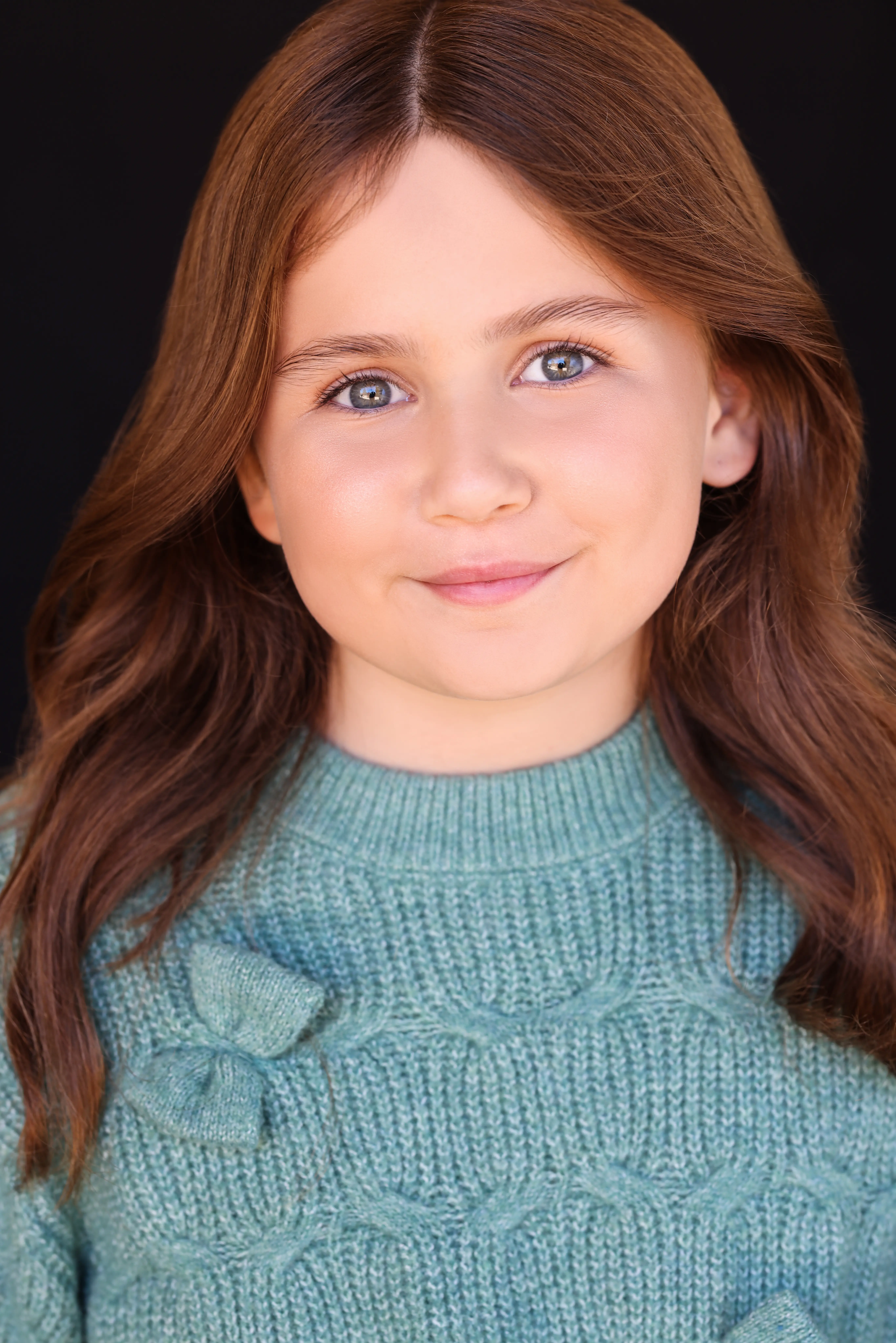 Child actress Caroline Brauner wearing a teal sweater with a confident expression against a black background