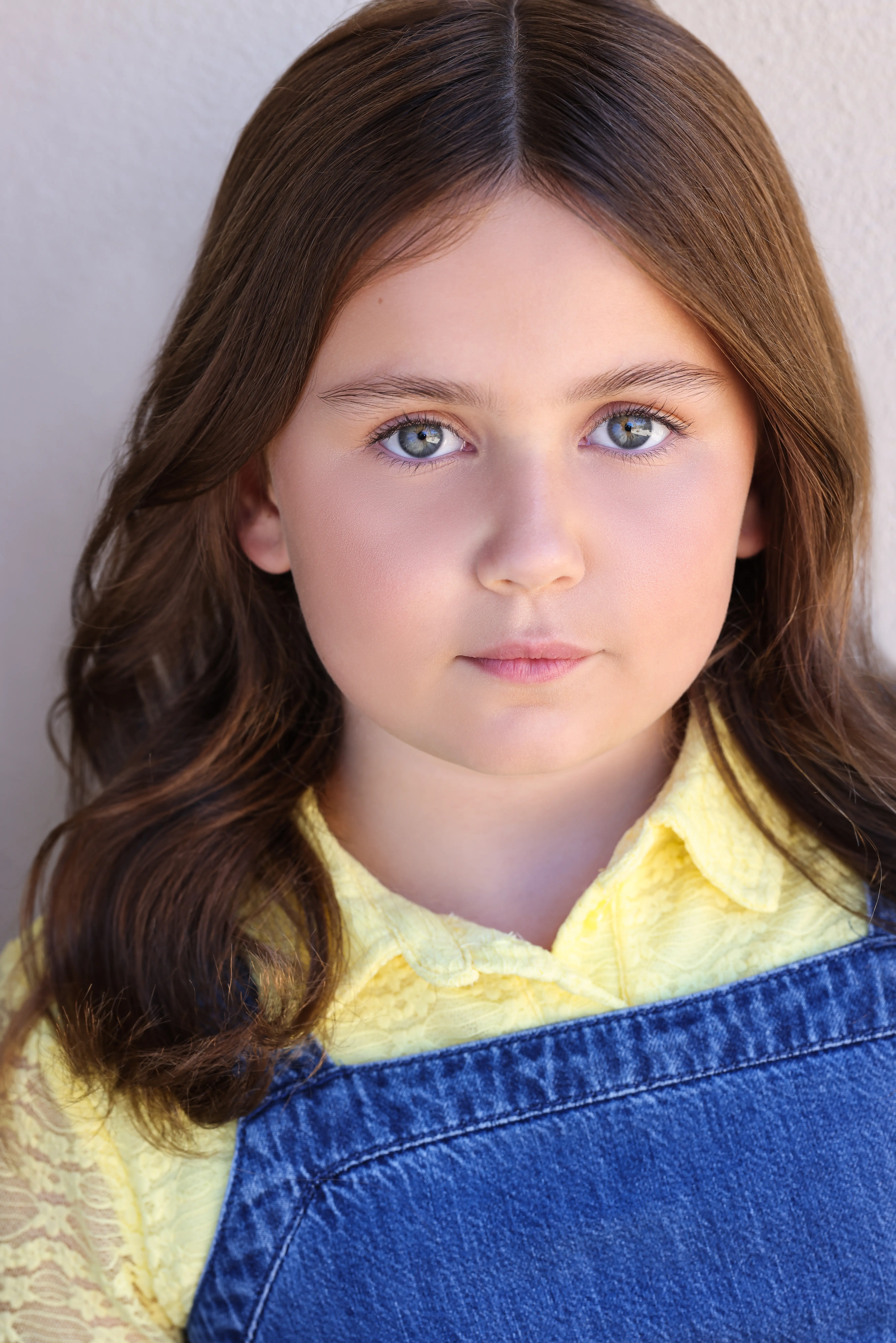 Child actress Caroline Brauner with a neutral expression wearing a yellow blouse and denim overalls