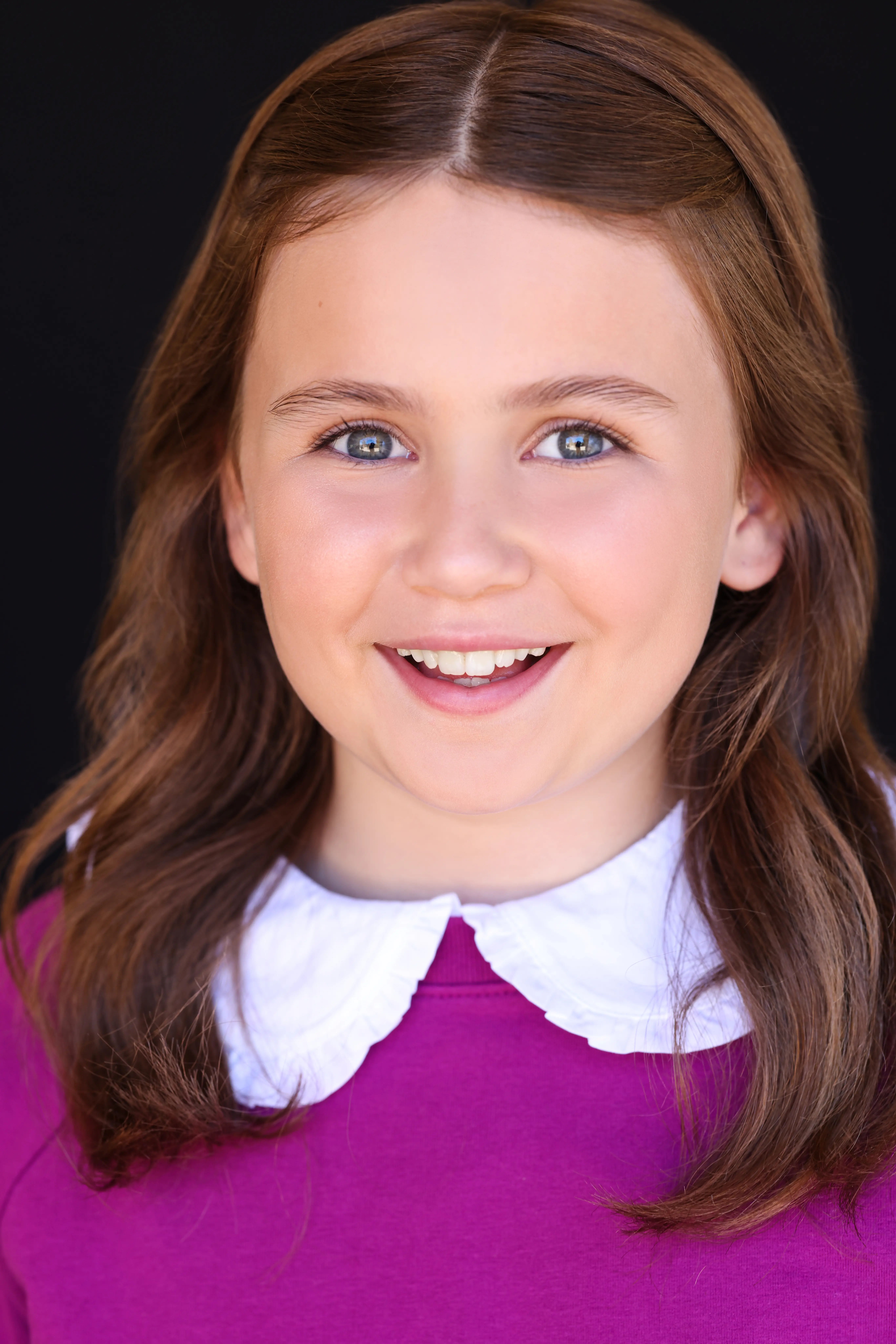 Child actress Caroline Brauner smiling in a purple dress with white collar against a black background