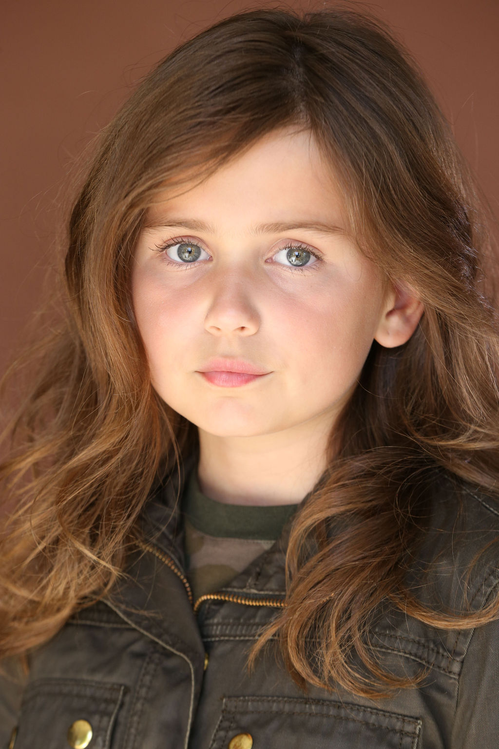 Close-up of Caroline Brauner with long brown hair and blue eyes wearing a dark green jacket against a brown background.