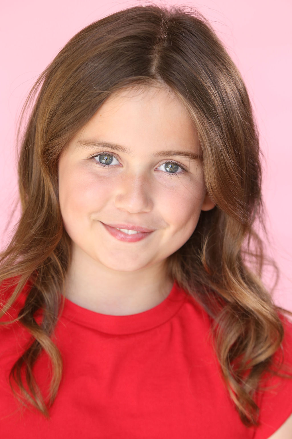 Smiling Caroline Brauner with wavy brown hair wearing a red shirt against a pink background.
