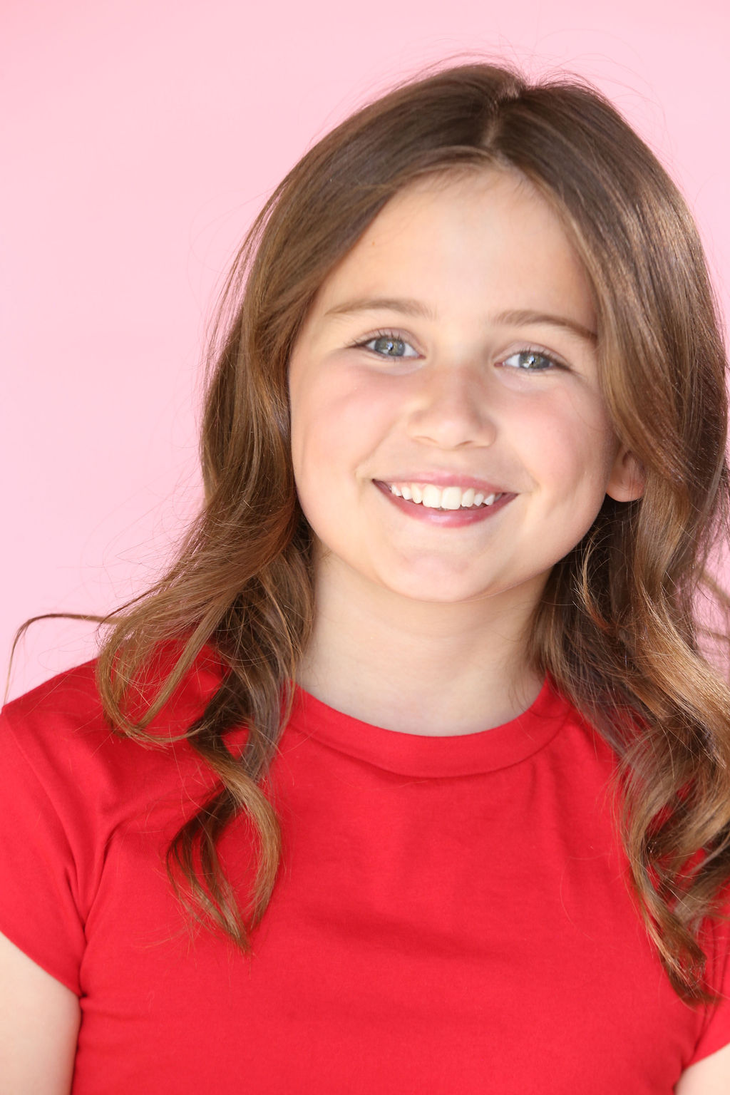 Smiling Caroline Brauner with wavy brown hair wearing a red shirt against a pink background.