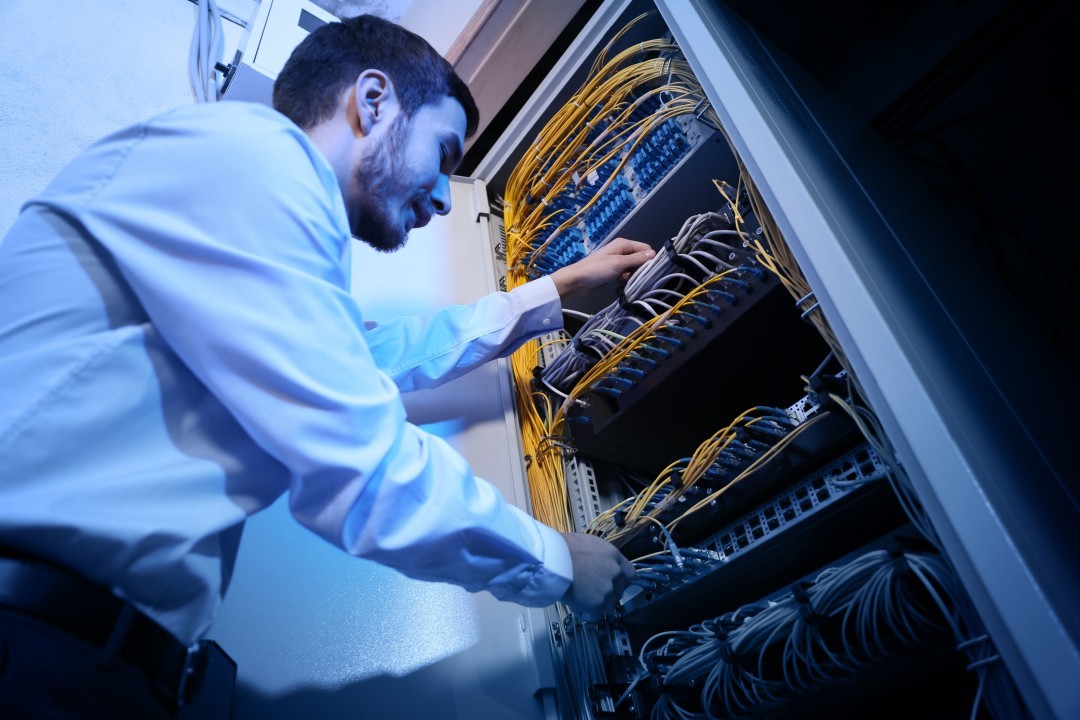 Technician working on a server rack with organized yellow and gray network cables in a data center.