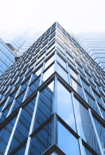 Green robotic vacuum cleaner operating on wooden floor in a bright living room with a sofa and glass coffee table.