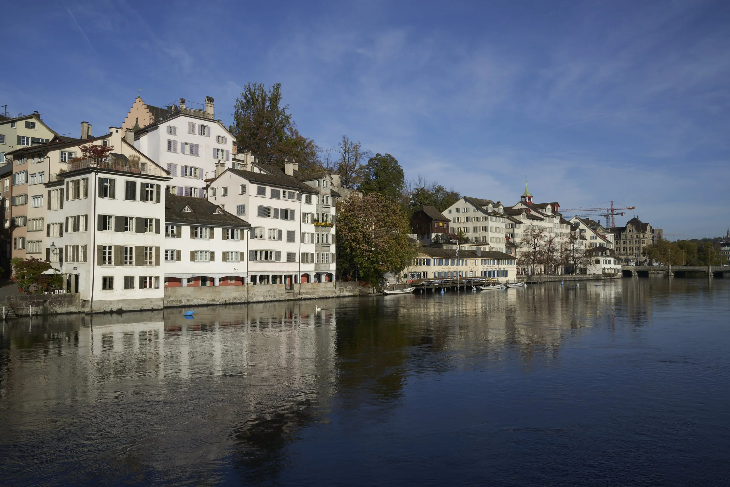 Waterfront view of traditional white buildings along a calm river under a blue sky in a European city.
