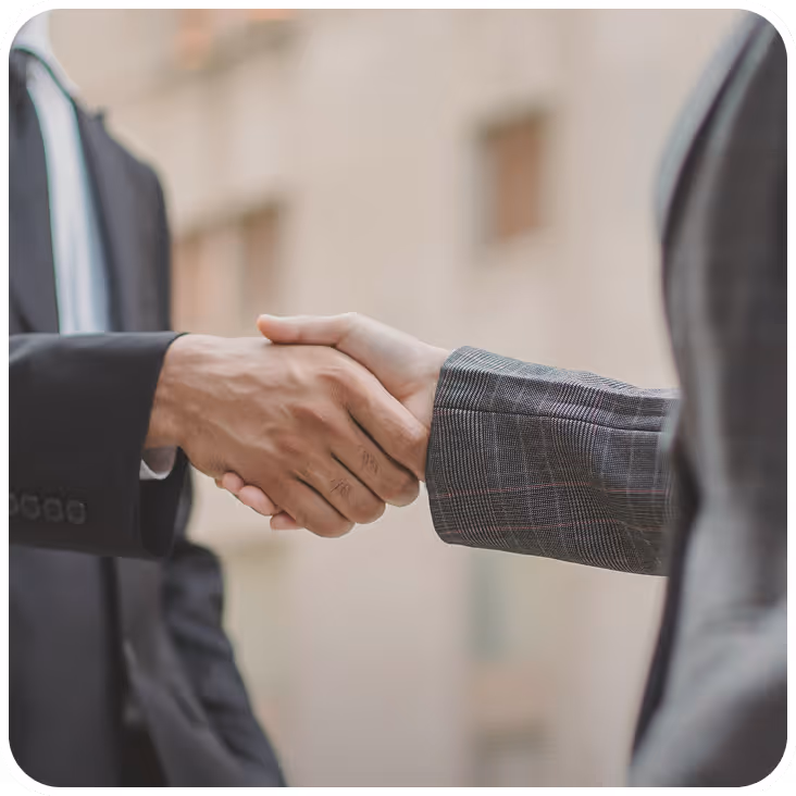 Close-up of two people shaking hands, one wearing a black suit and the other a gray checkered jacket.
