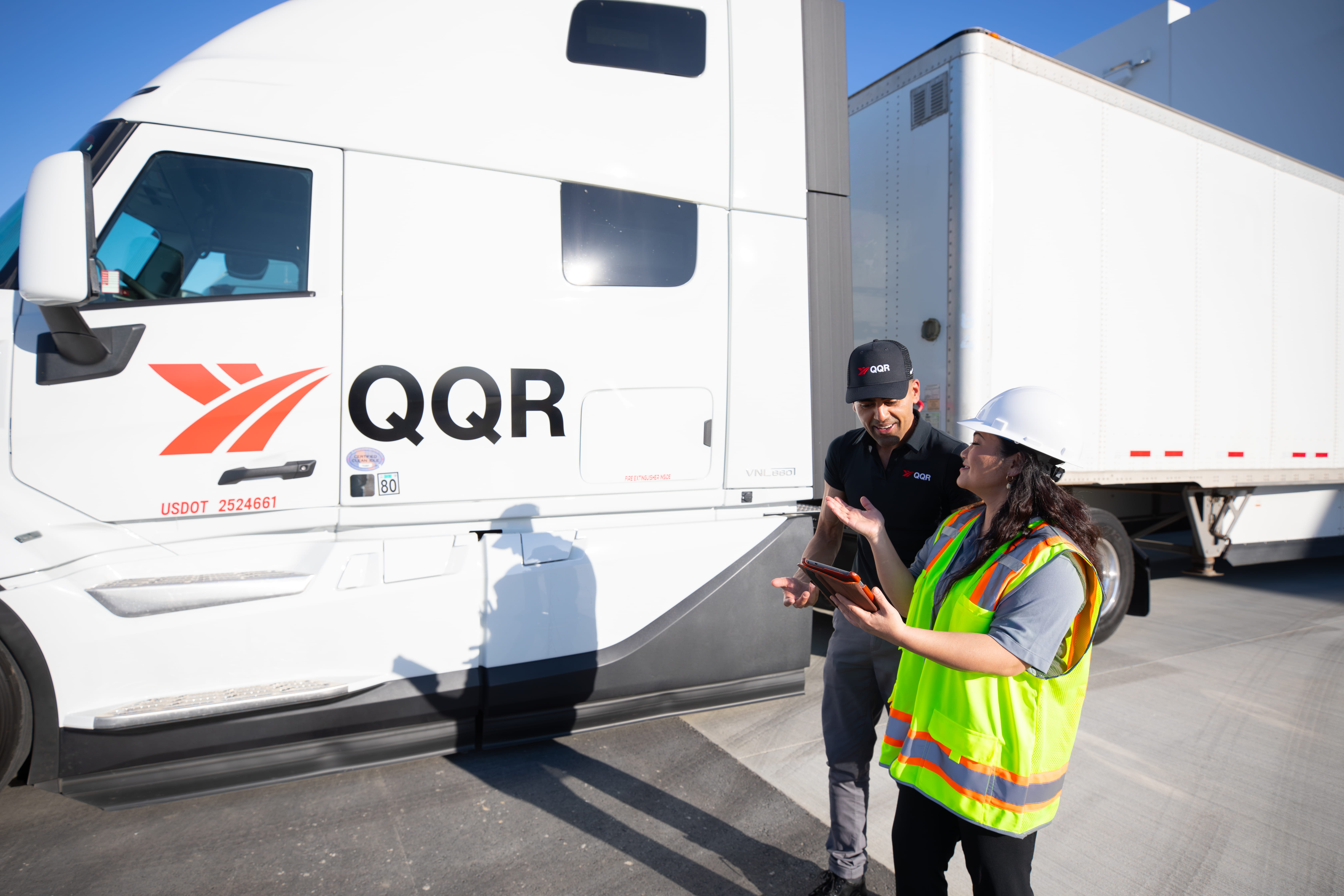 QQR truck driver and safety worker in high-visibility vest discussing near white commercial vehicle