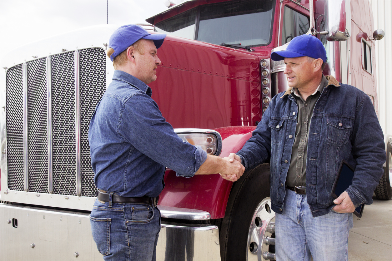 Two truck drivers shaking hands in front of red semi-truck outdoors