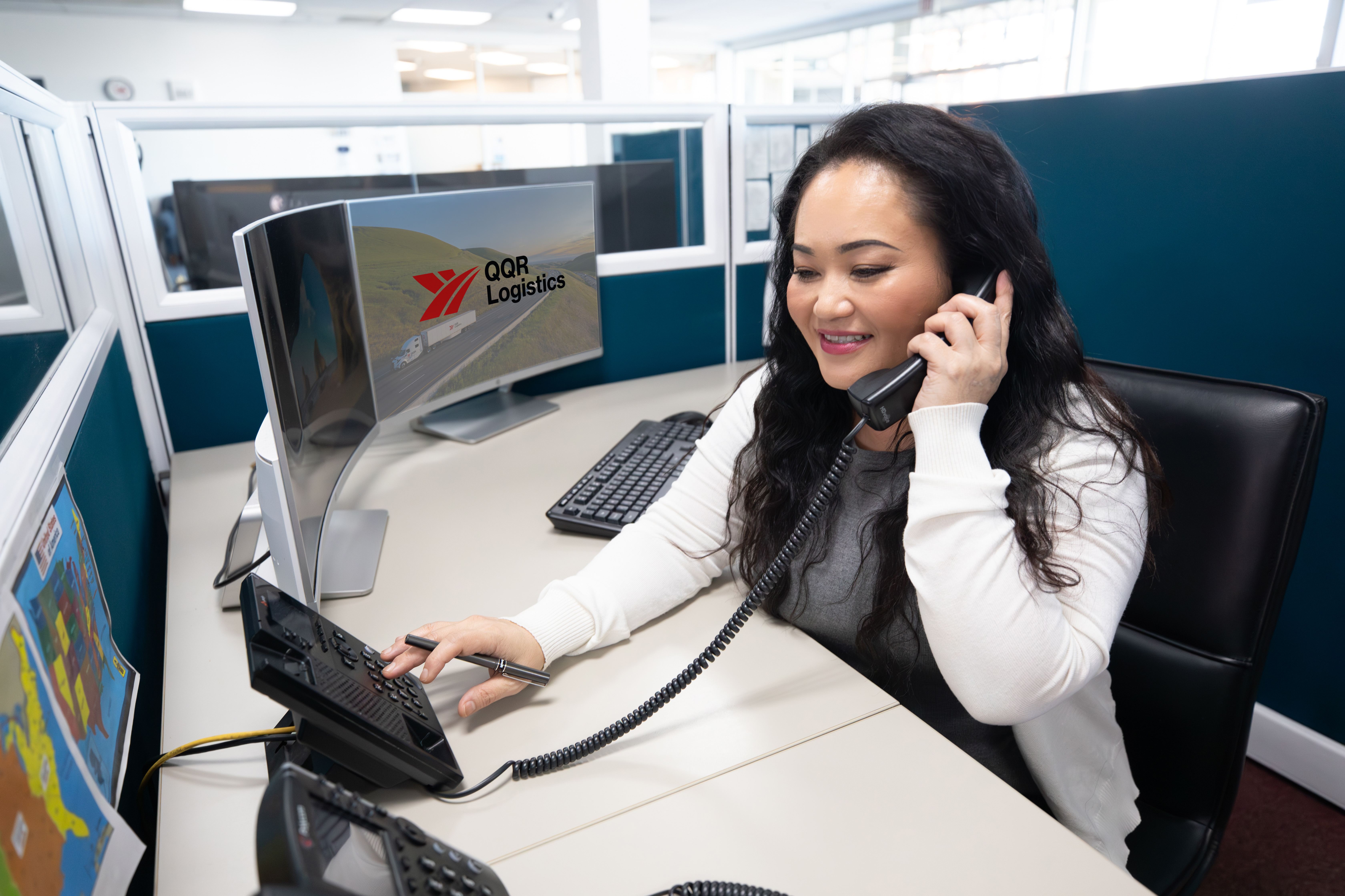 Woman at office desk on phone with QQR Logistics displayed on computer screen