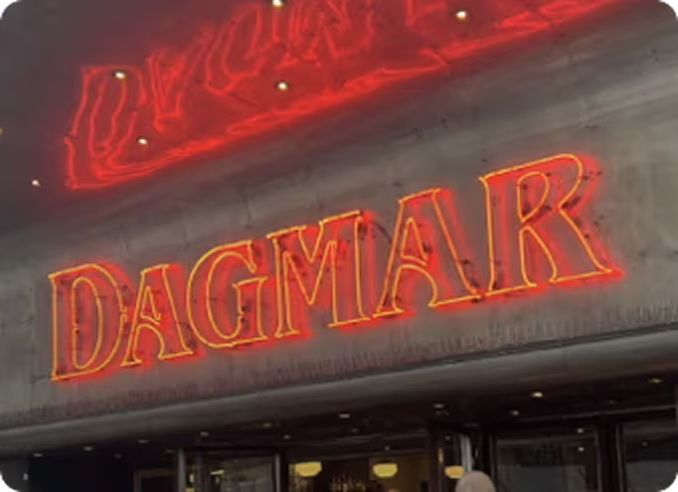 Red neon sign displaying the word 'DAGMAR' on a building facade.