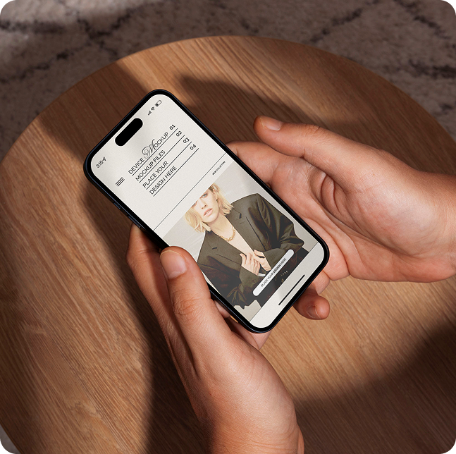 Hands holding a smartphone displaying a fashion app with a photo of a woman in a black blazer on a wooden surface.