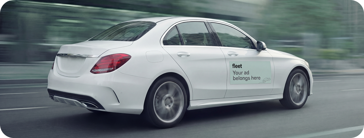 White sedan driving on a road with a sign on the rear door reading 'fleet Your ad belongs here'.